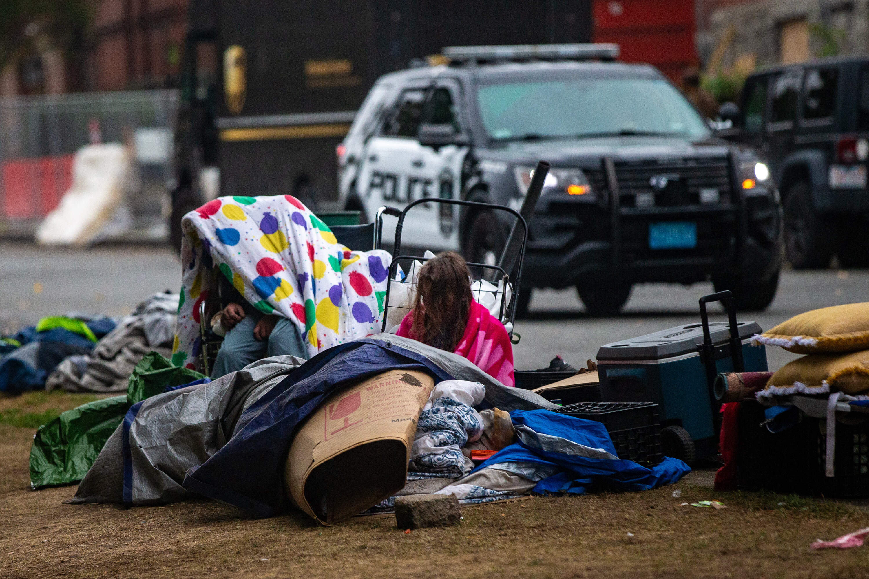 A woman sits among her belongings as the Lowell police and parks departments remove some items from a homeless encampment on South Common. (Jesse Costa/WBUR)