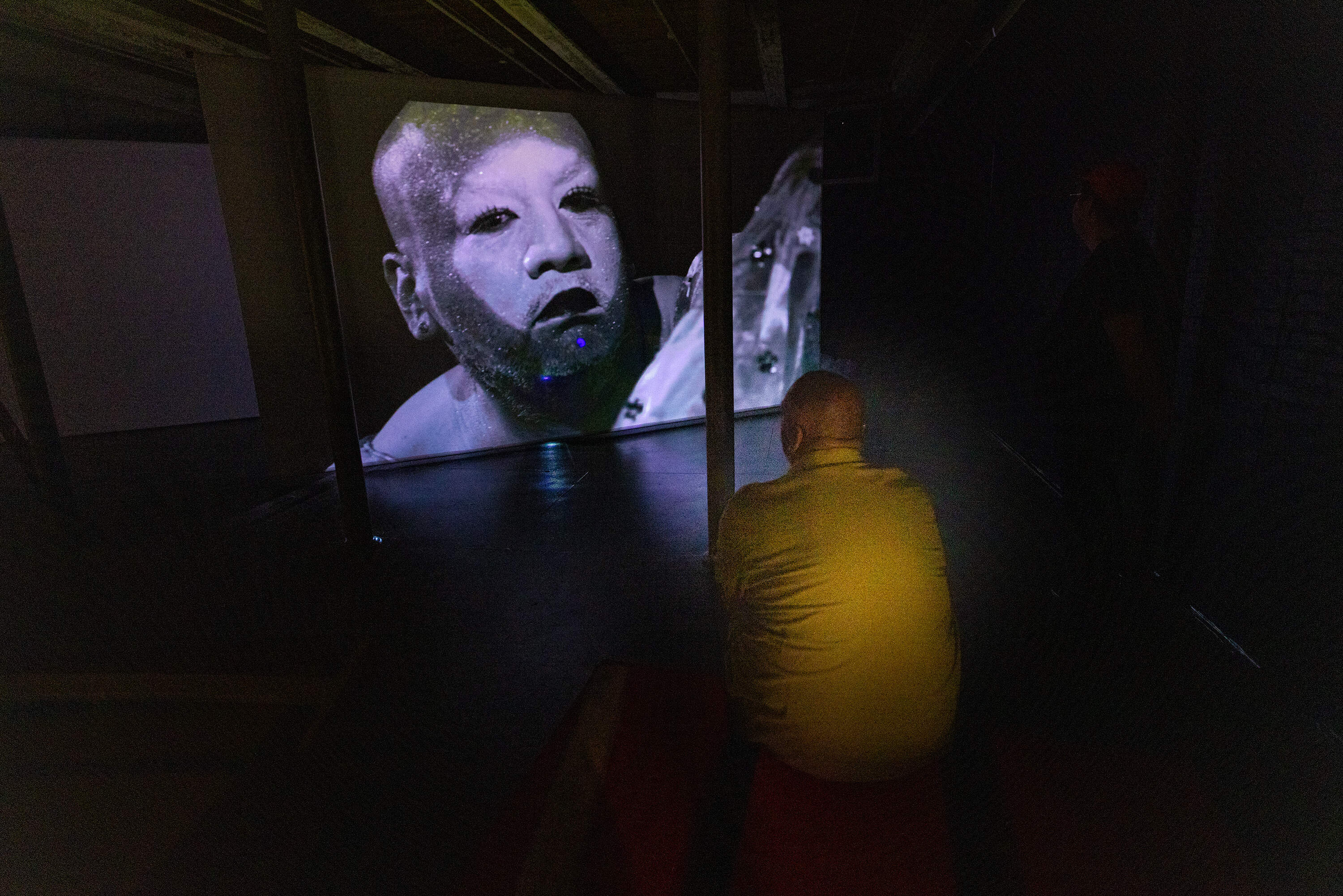 Jeffrey Gibson watches the video he produced in which he wears the seven garments from the exhibition. (Jesse Costa/WBUR)