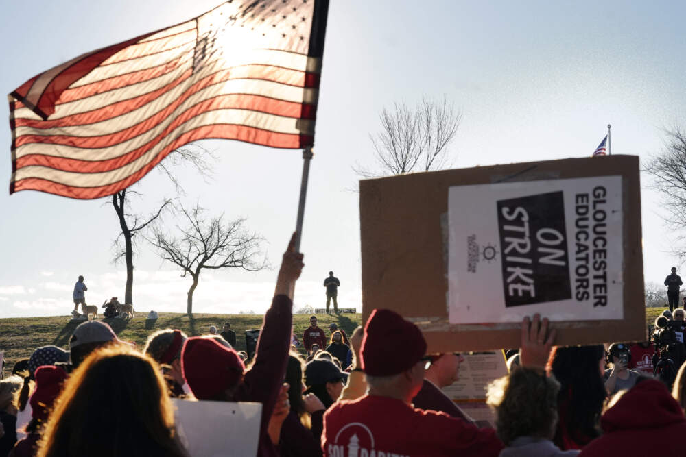 Teacher Andrea Swinson, of Gloucester, waves a flag, while teacher Eric Leigh, of Rockport, displays placard during a rally on Monday. (Steven Senne/AP)