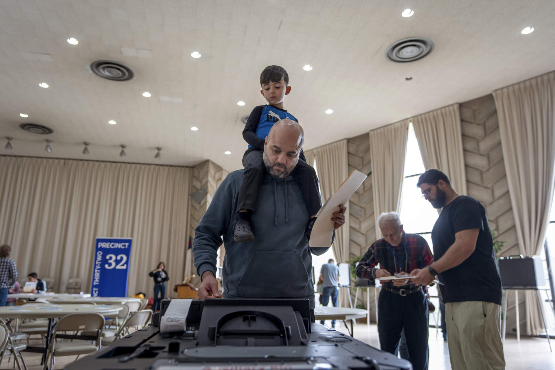 Three-year-old Zayn, sits on his father's shoulders as he inserts his ballot into a machine to vote at the First Presbyterian Church of Dearborn, in Dearborn, Mich. (David Goldman/AP)