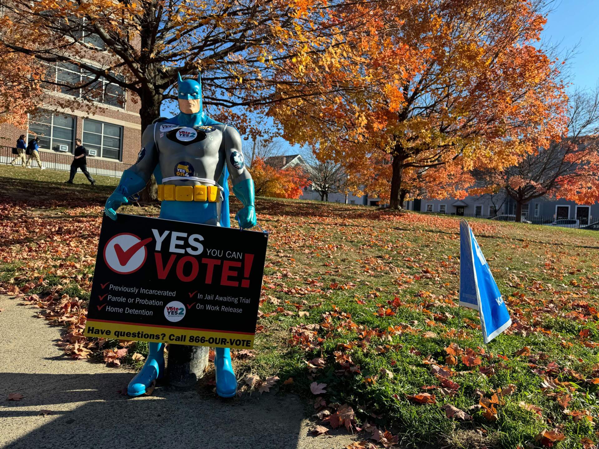 A Batman figurine stands outside East Boston High School with a voter information sign. (Walter Wuthmann/WBUR)