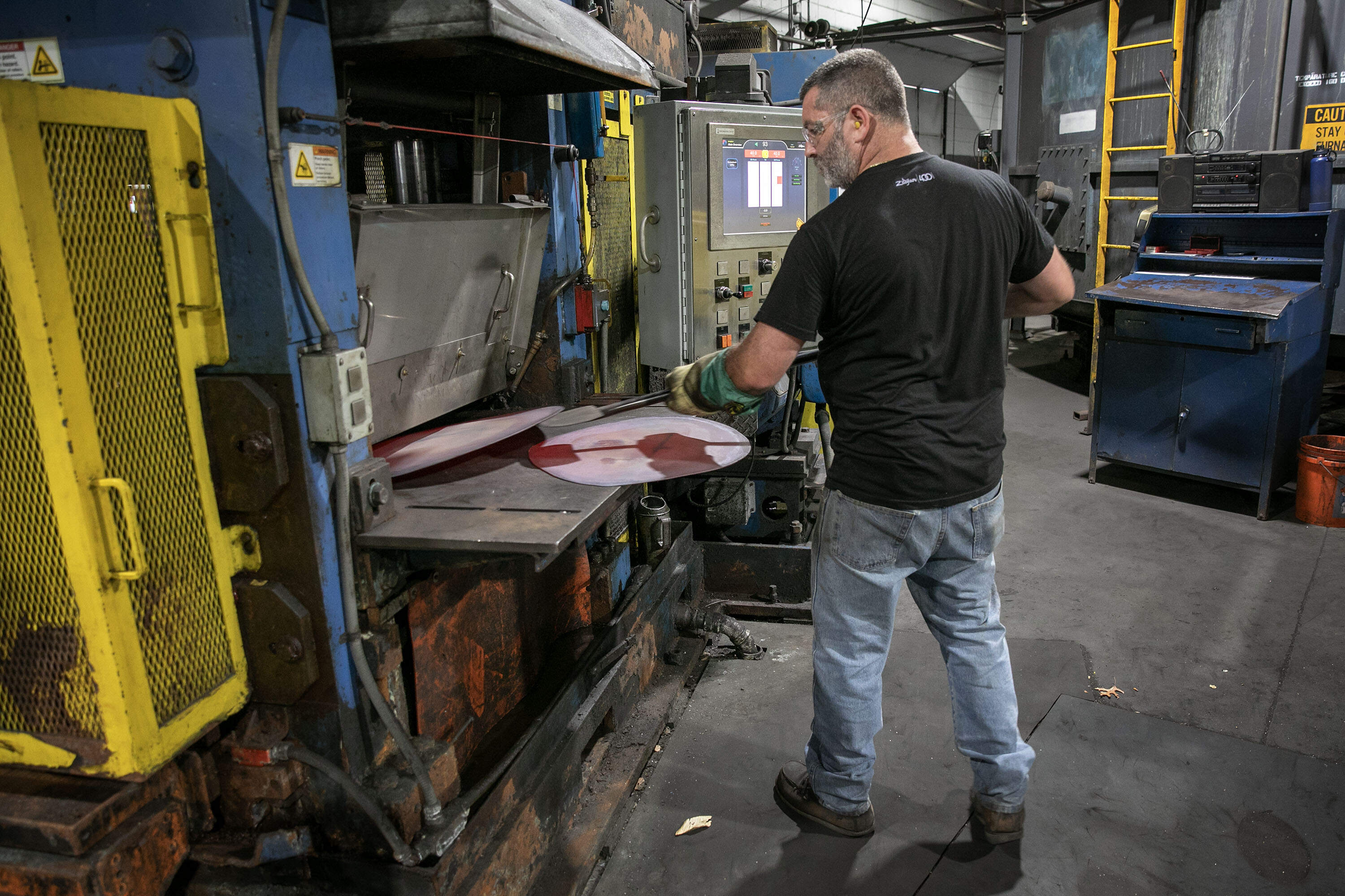 Mill operator Matt Fraser feeds disks of hot metal into a roller at the Zildjian cymbal factory. (Robin Lubbock/WBUR)