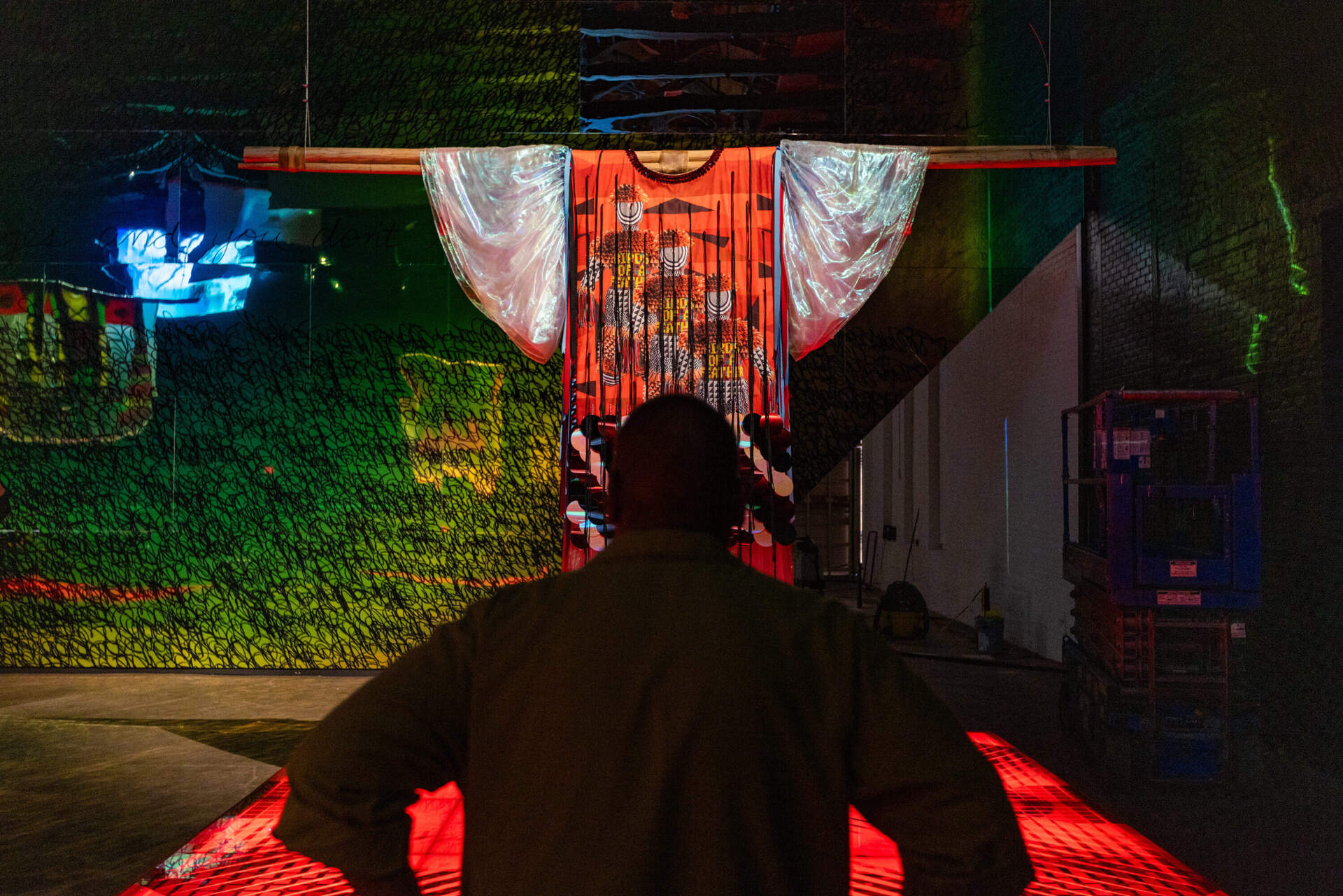 Jeffrey Gibson looks at one of the large garments suspended over a 12 x 12-foot stage in the front gallery titled, 'Your Spirit Whispers in My Ear" part of his upcoming exhibit, "Power Full Because We're Different" in the largest space at Mass MoCA.