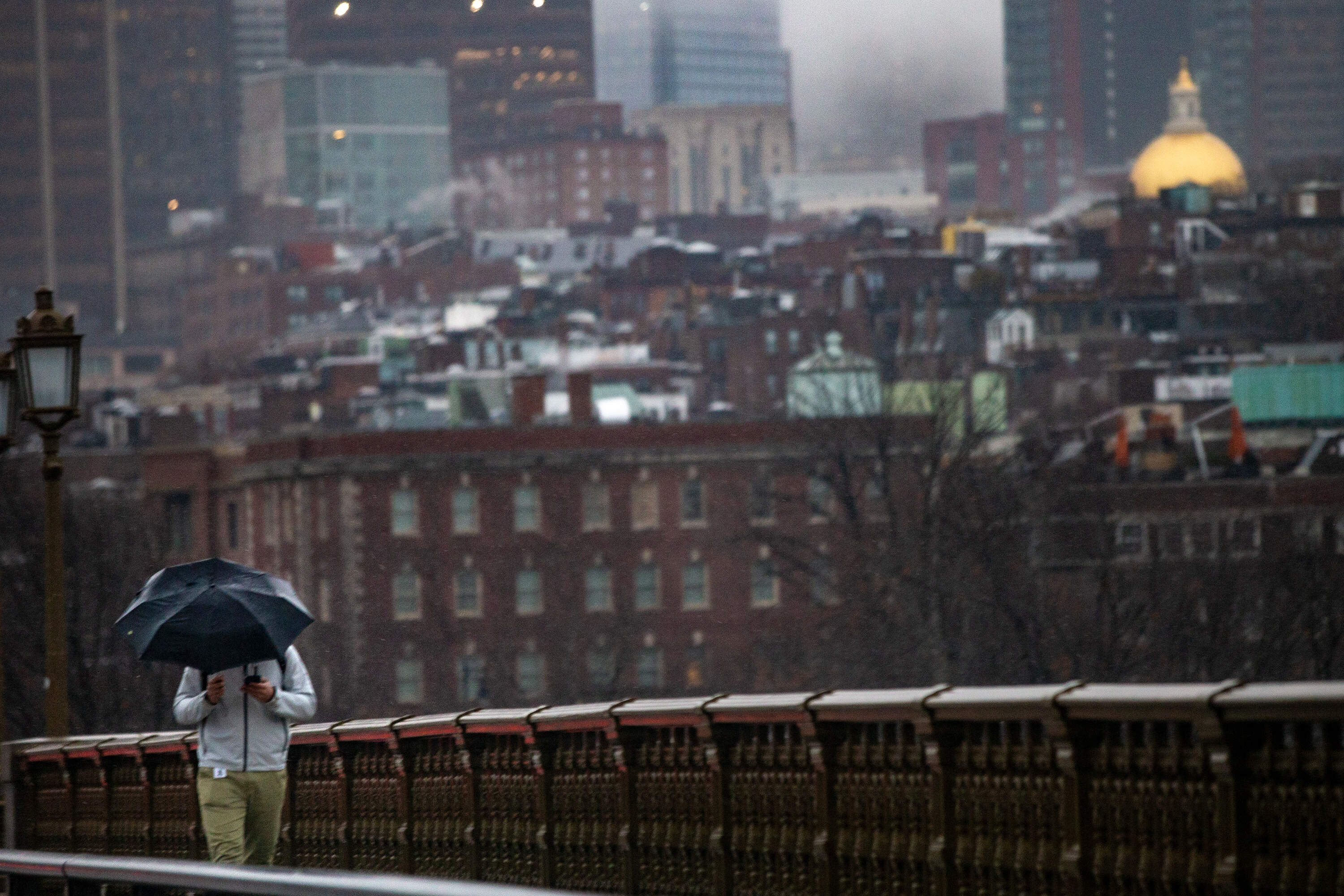 A man with an umbrella walks over the Longfellow Bridge during the rain storm on Dec. 11, 2024. (Jesse Costa/WBUR)