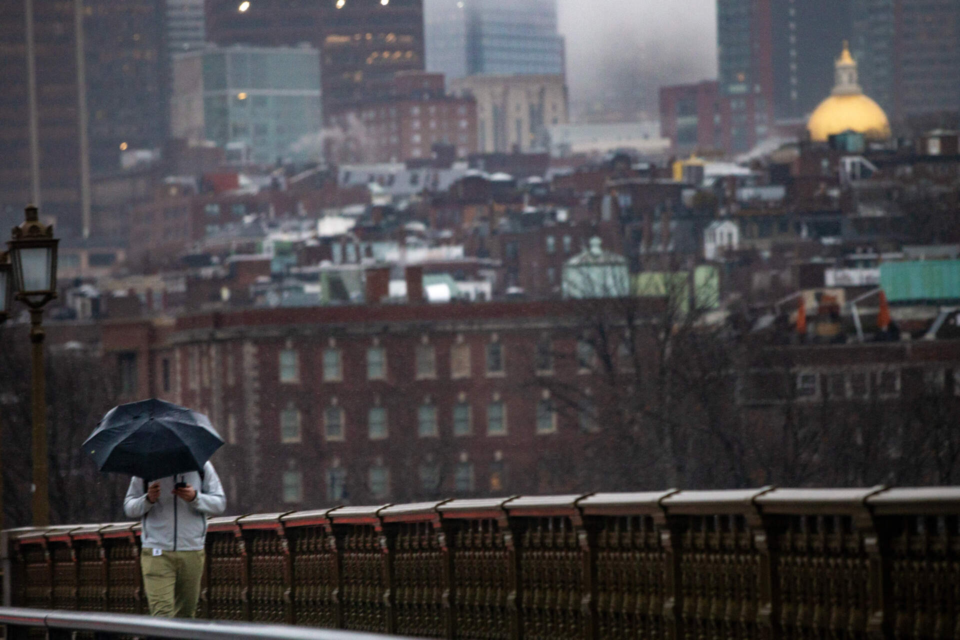 A man with an umbrella walks over the Longfellow Bridge in the morning during the winter storm.