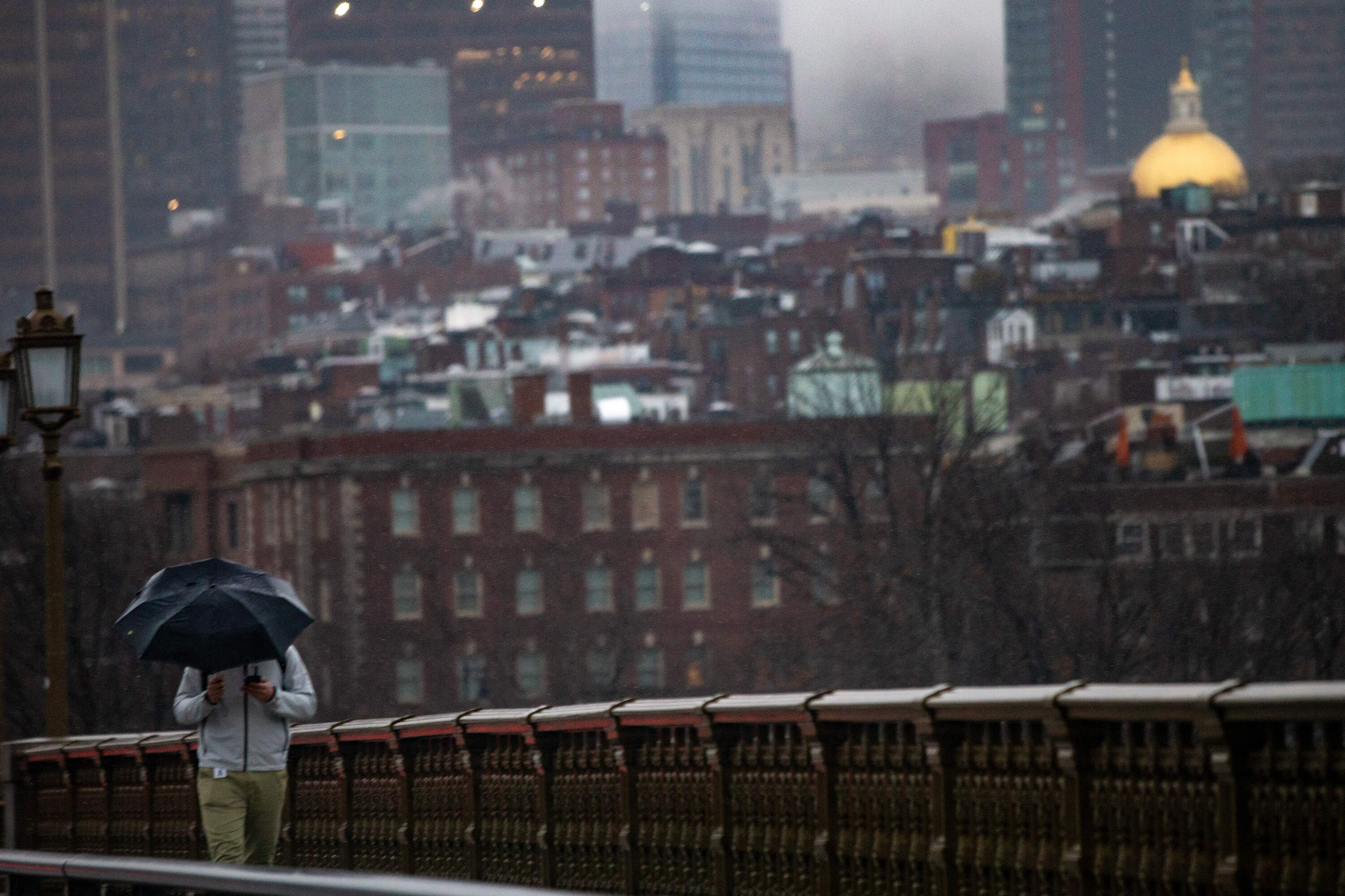 A man with an umbrella walks over the Longfellow Bridge during the rain storm on Dec. 11, 2024. (Jesse Costa/WBUR)