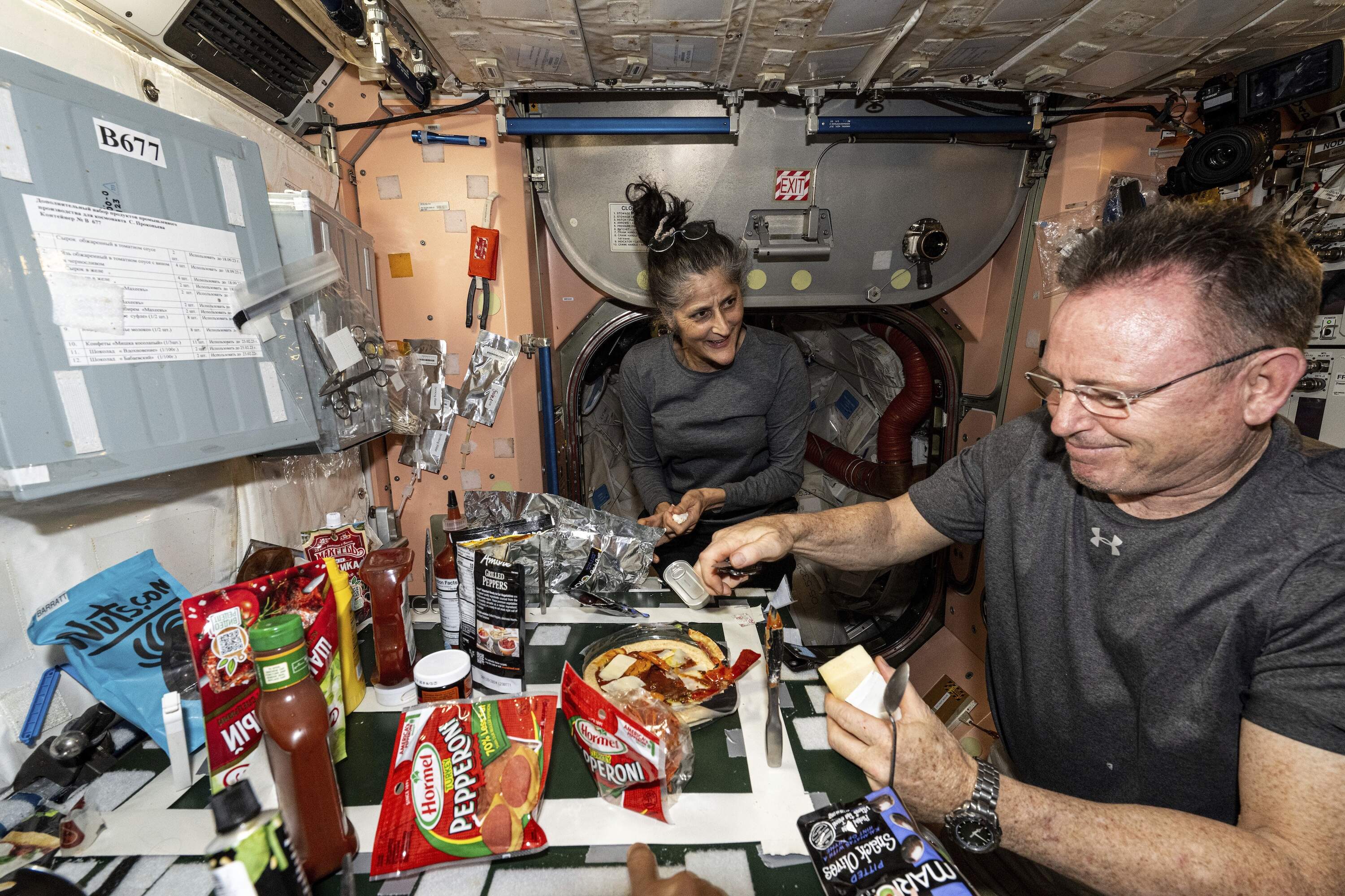 In this image released by NASA, NASA astronauts Suni Williams and Butch Wilmore, both Expedition 71 Flight Engineers, make pizza aboard the International Space Station's galley located inside the Unity module on Sept. 9, 2024. Items are attached to the galley using tape and velcro to keep them from flying away in the microgravity environment. (NASA via AP, File)
