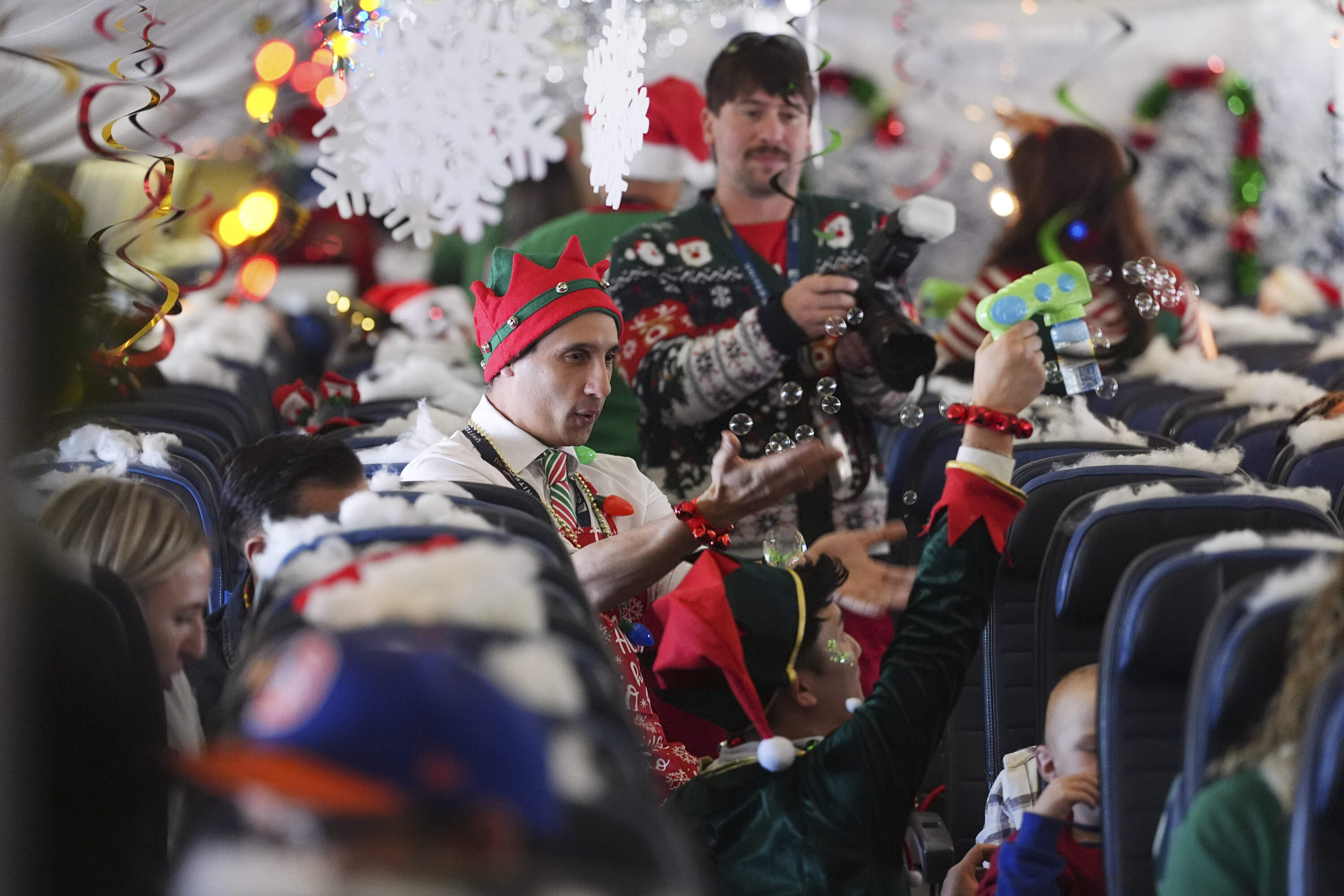 Flight attendant Gustavo Oliveira, center, juggles bubbles to entertain passengers during the United Airlines annual "fantasy flight" to a fictional North Pole at Denver International Airport, Saturday, Dec. 14, 2024. (David Zalubowski/AP)
