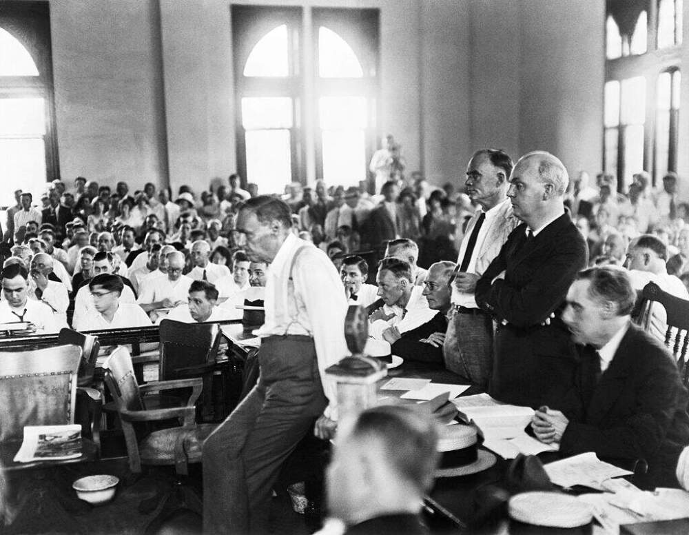 Defense attorney Clarence Darrow leans against a table during the Scopes "Monkey" Trial in which biology teacher John T. Scopes was prosecuted for teaching evolution to his class. Scopes is seated to Darrow's right with his arms folded. (Getty Images)