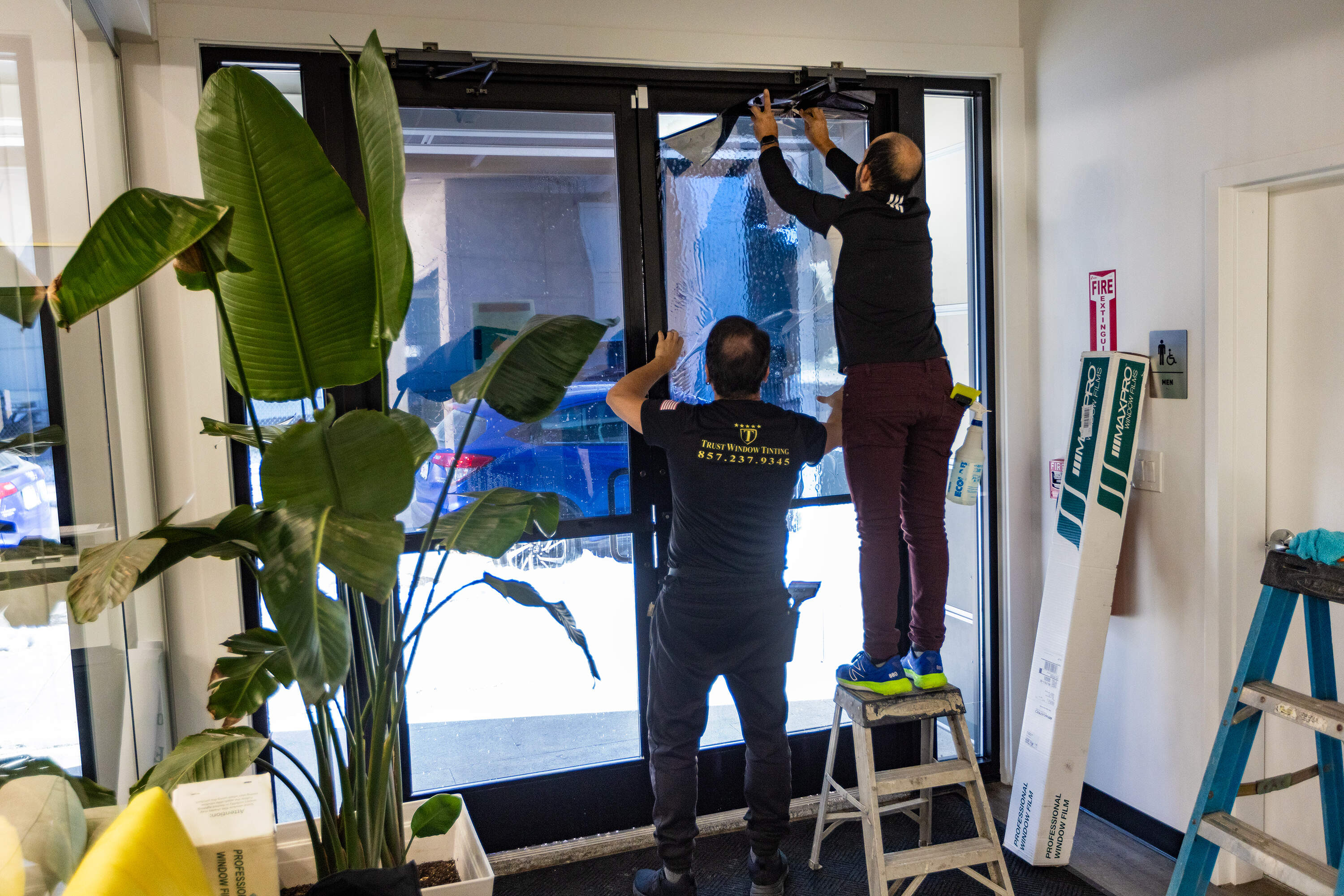 Workers at La Colaborativa in Chelsea install tinted window film on a doorway for security. (Jesse Costa/WBUR)