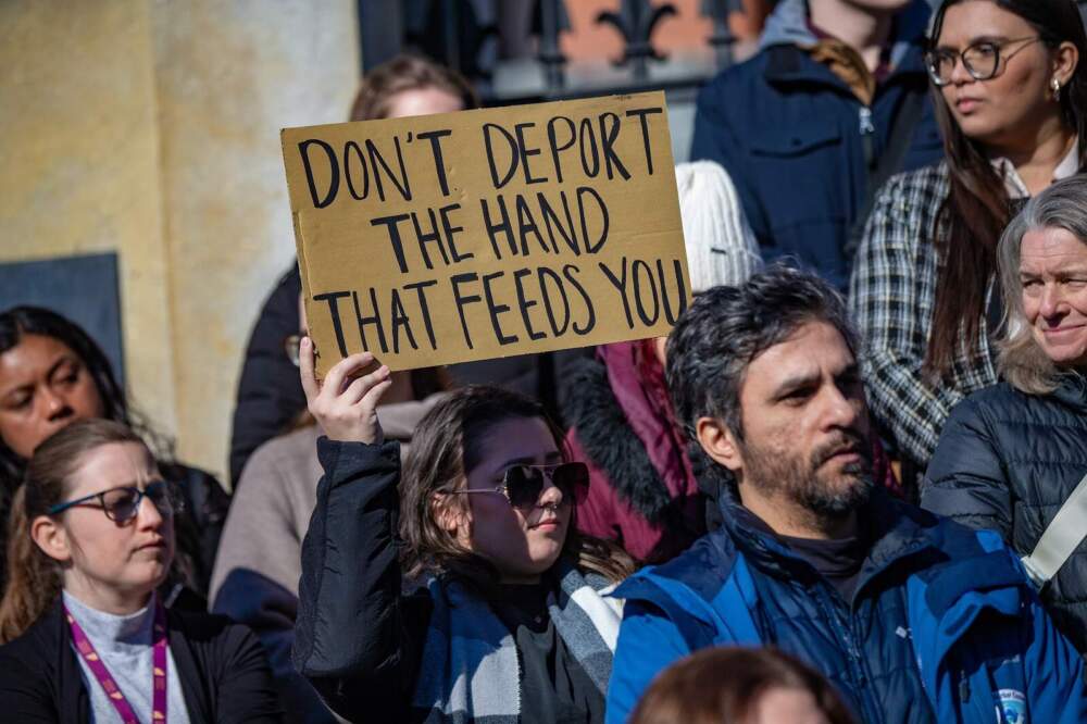 A rally participant holds a sign reading “Don’t Deport the Hand That Feeds You” during the MIRA rally at the State House Jan. 29, 2025. (Jesse Costa/WBUR)