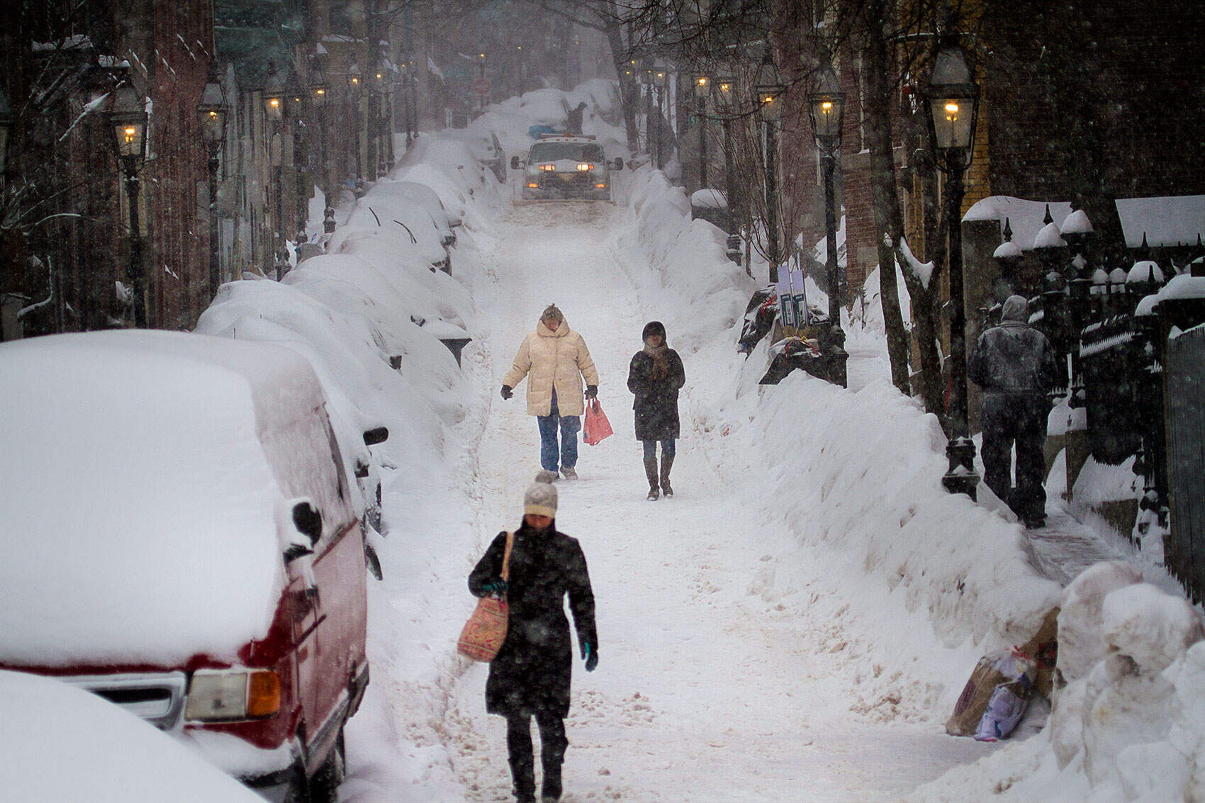 A plow rolls down the street as people trudge forward through the snow on Joy Street in Boston’s Beacon Hill neighborhood on Feb. 9, 2015. (Jesse Costa/WBUR)