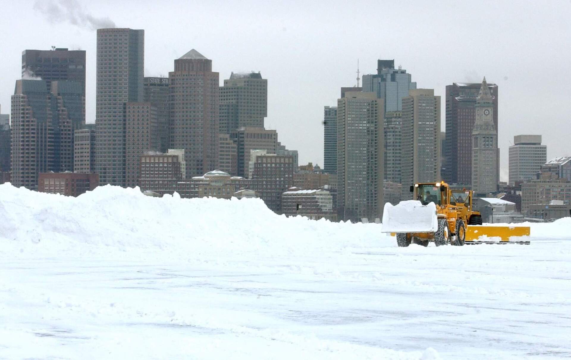 Snow is cleared from the south cargo area of Logan Airport with Boston as a backdrop following a blizzard Tuesday, Feb. 18, 2003 in Boston. (Lisa Poole/AP)