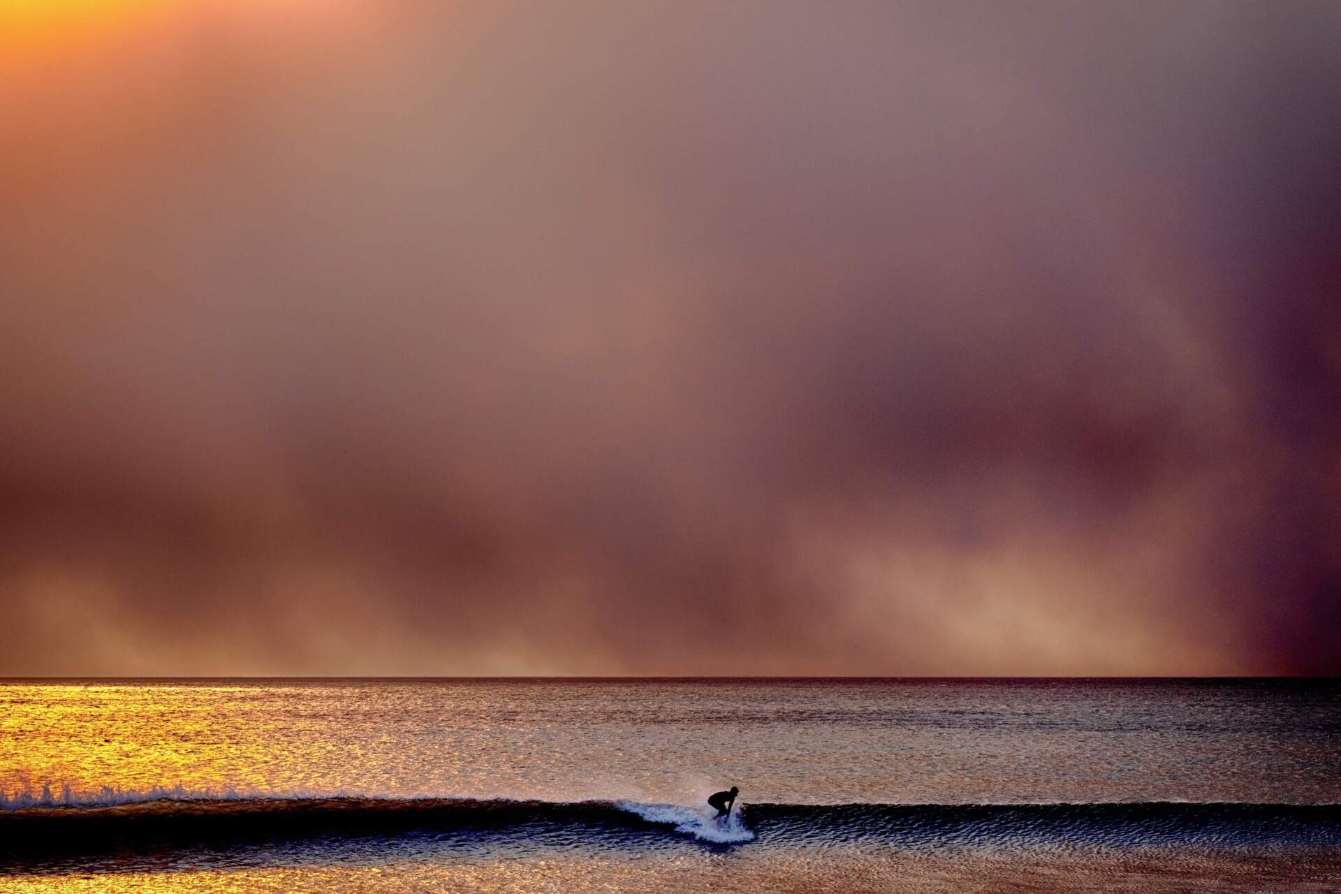 A surfer takes off on a wave in Santa Monica, Calif., during sunset under a blackened sky from the Palisades fire in the Pacific Palisades on Tuesday, Jan. 7, 2025. (Richard Vogel/AP)