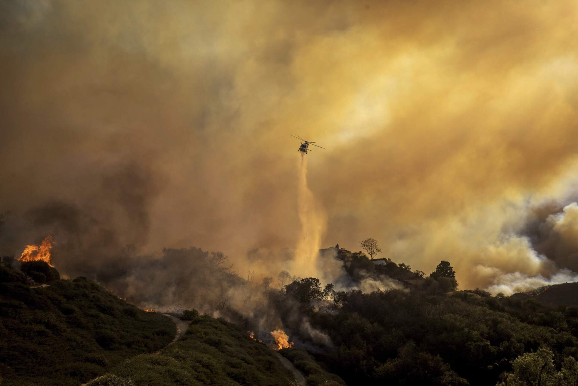 Water is dropped on the advancing Palisades Fire by helicopter in the Pacific Palisades neighborhood on Tuesday. (Ethan Swope/AP)