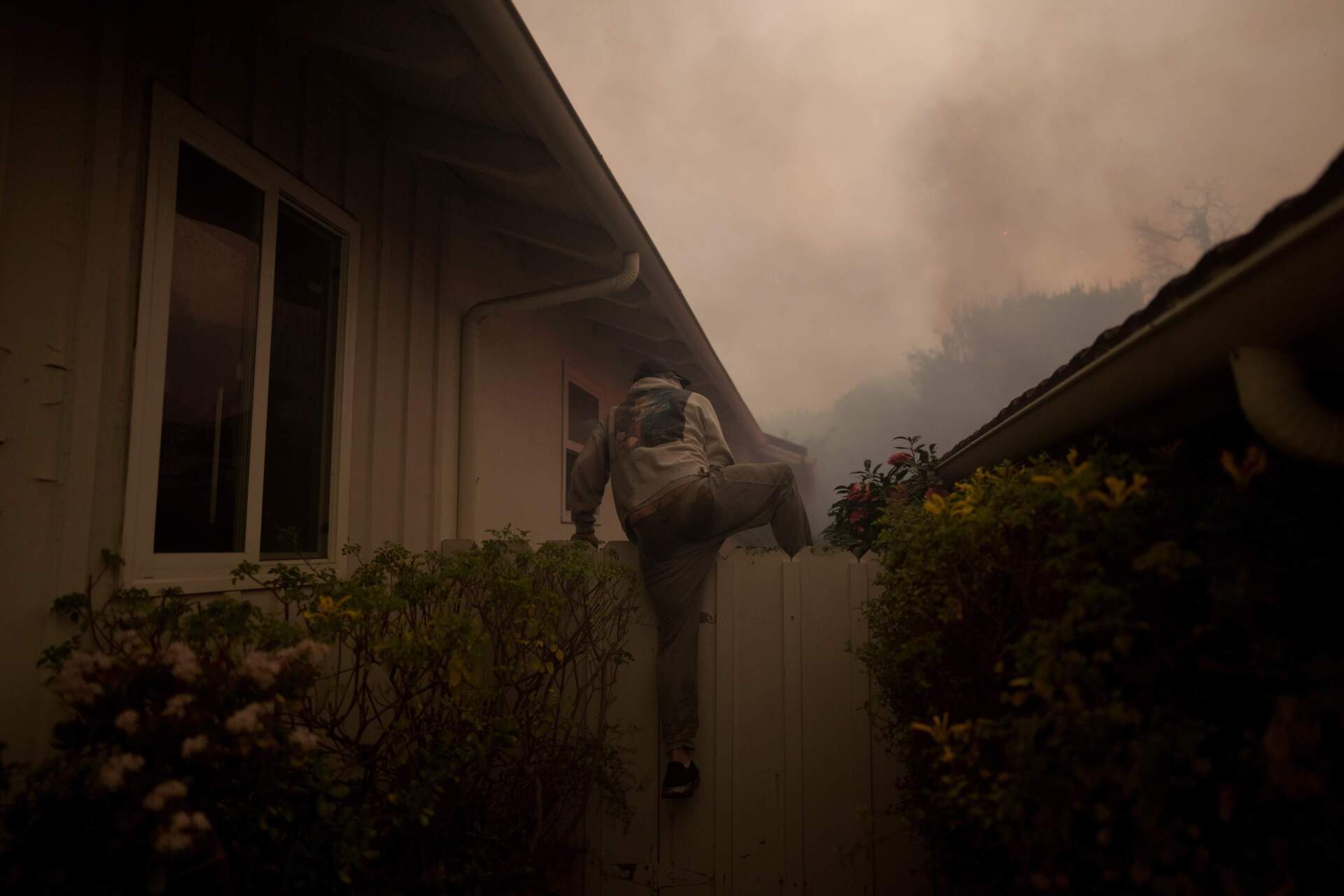 A resident climbs a fence to check on a home as flames from the Palisades Fire approach on Tuesday in the Pacific Palisades neighborhood. (Eric Thayer/Getty Images)