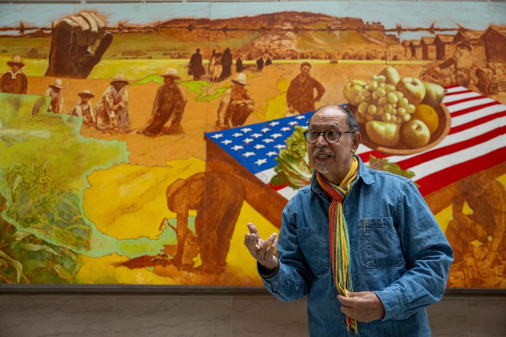Muralist Carlos Hernández Chávez stands before his work, “Sugar Beet Workers” in the atrium of Hartford City Hall on December 16, 2024. (Tyler Russell/Connecticut Public)