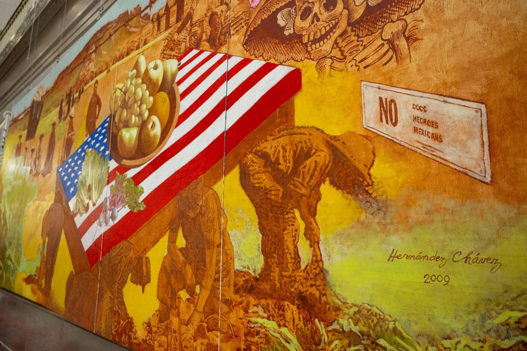 Beside the workers bearing the American table on their backs is a sign that reads “No Dogs, Negroes, Mexicans”. Chávez commented that even in discrimination “we are third on the list.” (Tyler Russell/Connecticut Public)