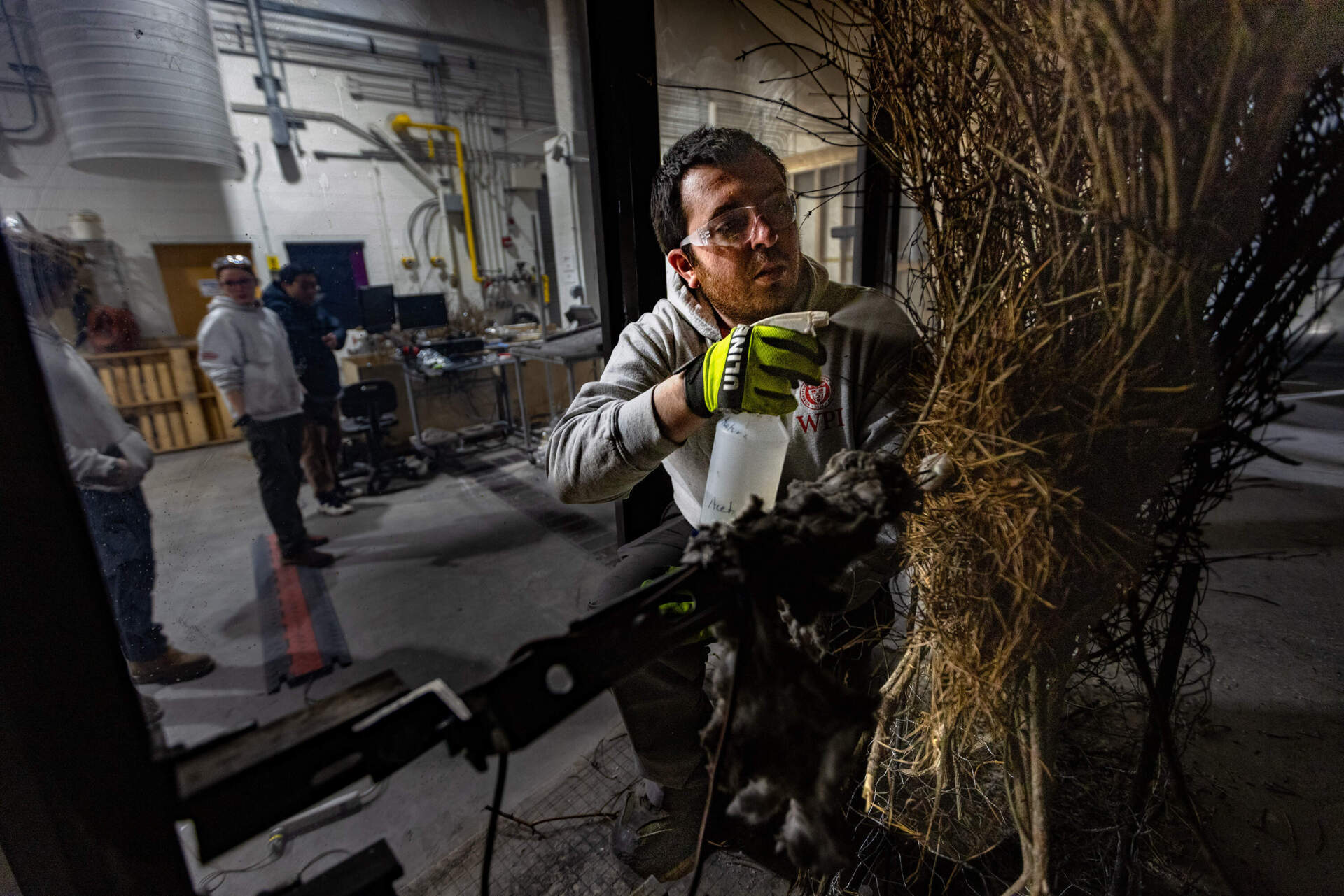 Fernando Ebensperger, a doctoral student in the fire protection engineering department at WPI, sprays accelerant on brush inside the wind tunnel. (Jesse Costa/WBUR)