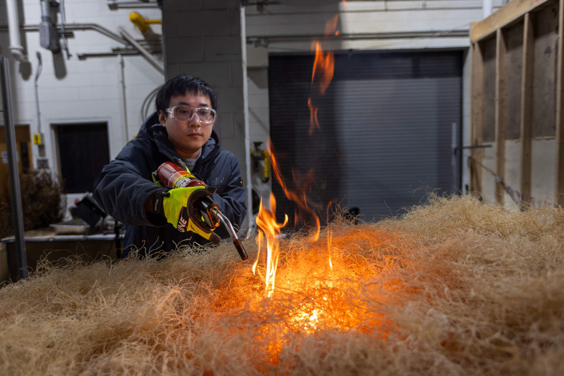 Xiuqi Xi, a postdoctoral fellow at WPI, sets fire to the center of a tilted table filled with brush, to test how a burning fire reacts to an incline and the effects of gravity. (Jesse Costa/WBUR)