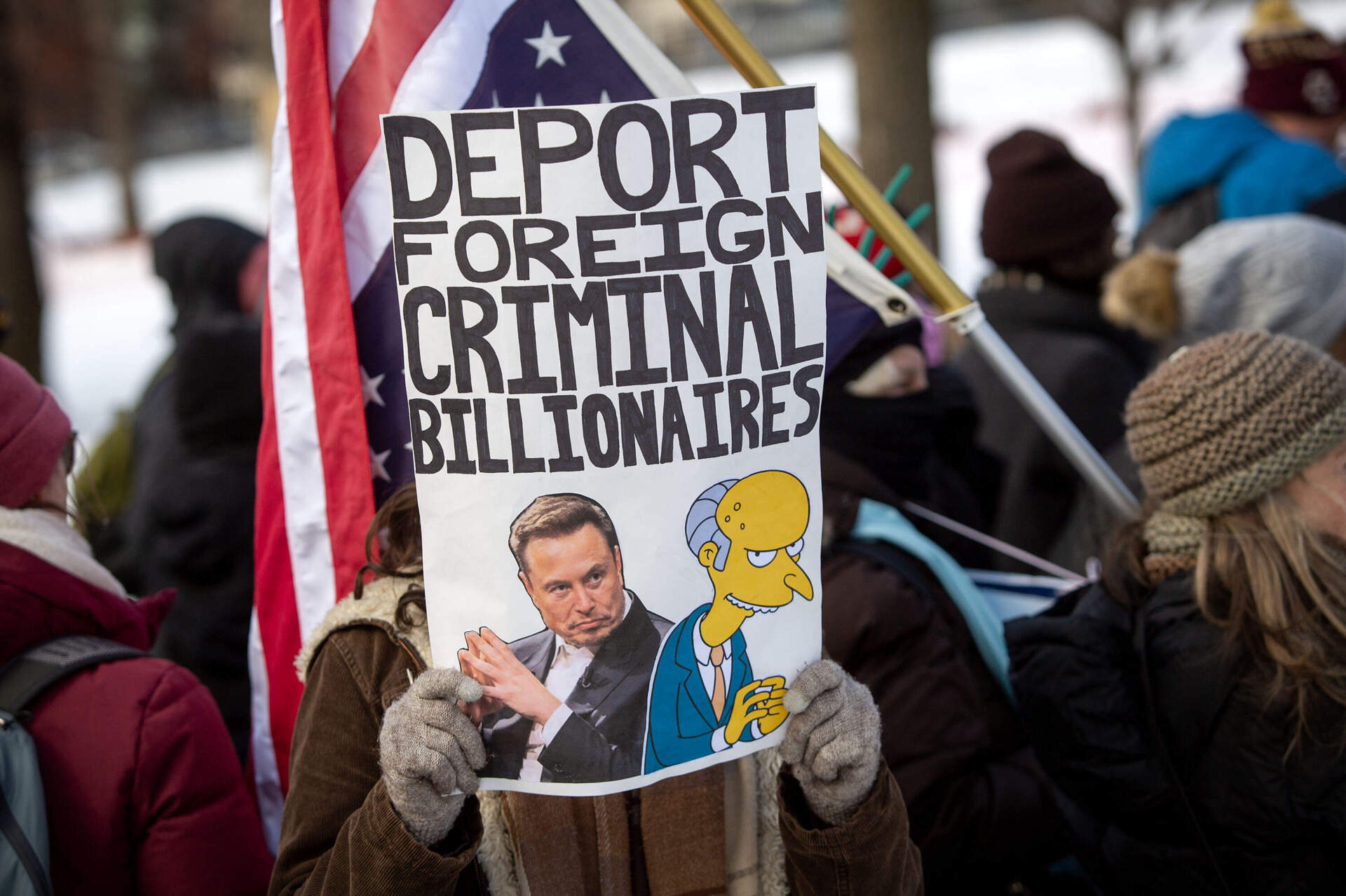 A protester at the "No Kings on Presidents' Day" rally and march, holds up a sign saying "deport foreign criminal billionaires" with a picture of Elon Musk. (Robin Lubbock/WBUR)