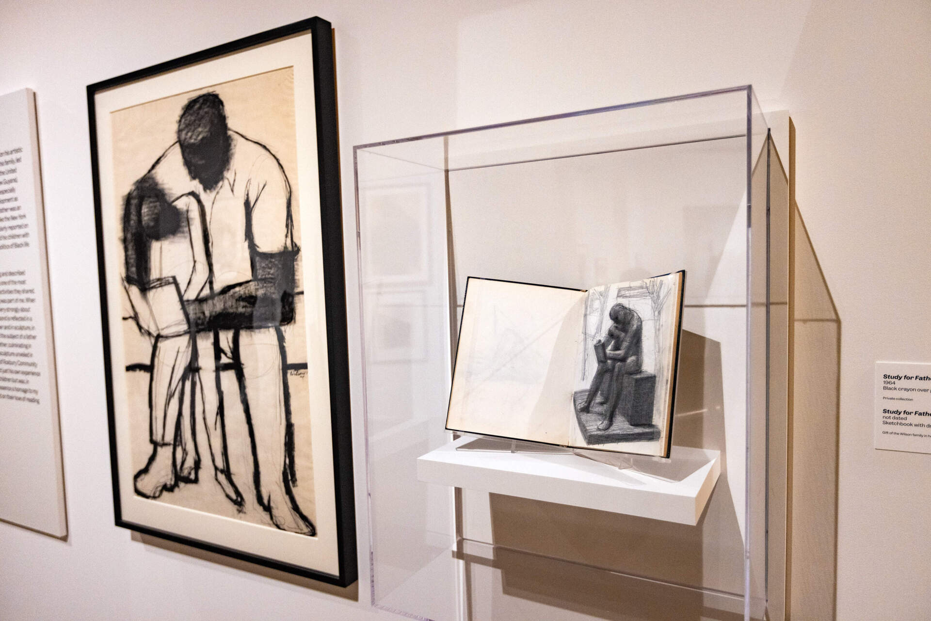 The black crayon and sketchbook drawings of “Father and Child Reading” at the “Witnessing Humanity: The Art of John Wilson” exhibit at the Museum of Fine Arts, Boston. Later, a large-scale bronze sculpture was unveiled in 1990 at the campus of Roxbury Community College. (Jesse Costa/WBUR)