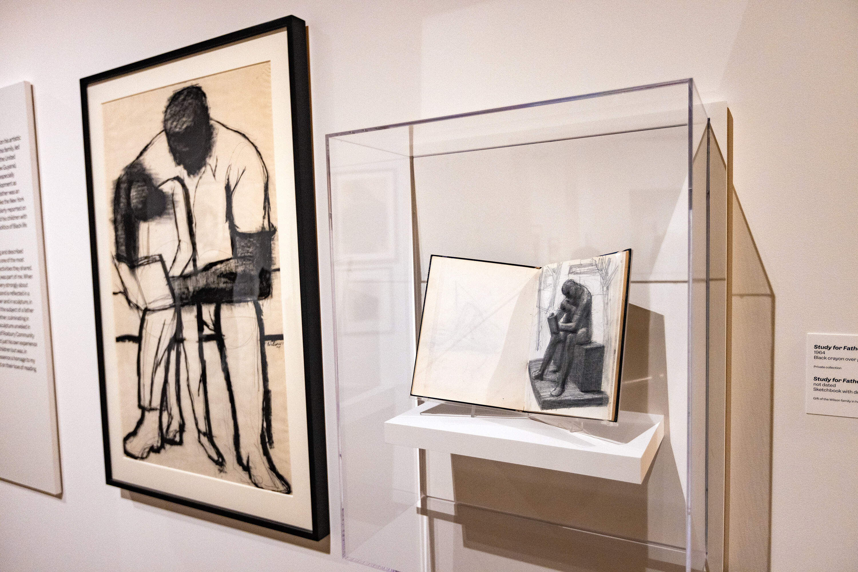 The black crayon and sketchbook drawings of “Father and Child Reading” at the “Witnessing Humanity: The Art of John Wilson” exhibit at the Museum of Fine Arts, Boston. Later, a large-scale bronze sculpture was unveiled in 1990 at the campus of Roxbury Community College. (Jesse Costa/WBUR)
