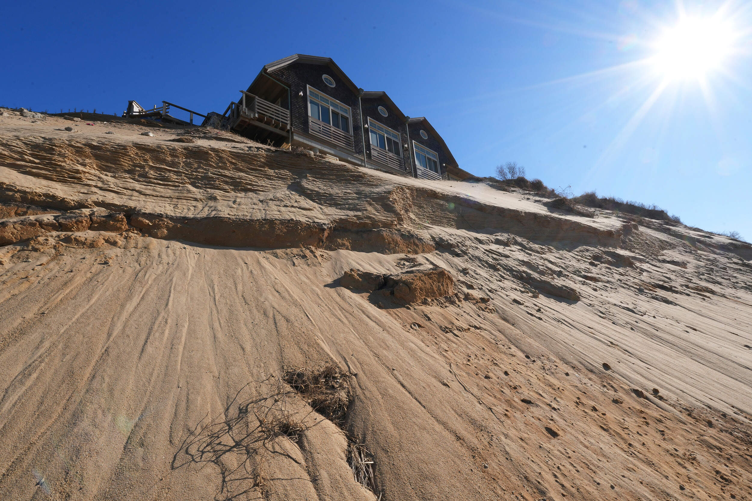 Sand slopes down from beneath a house on the dunes. (Andre Muggiati/AP)