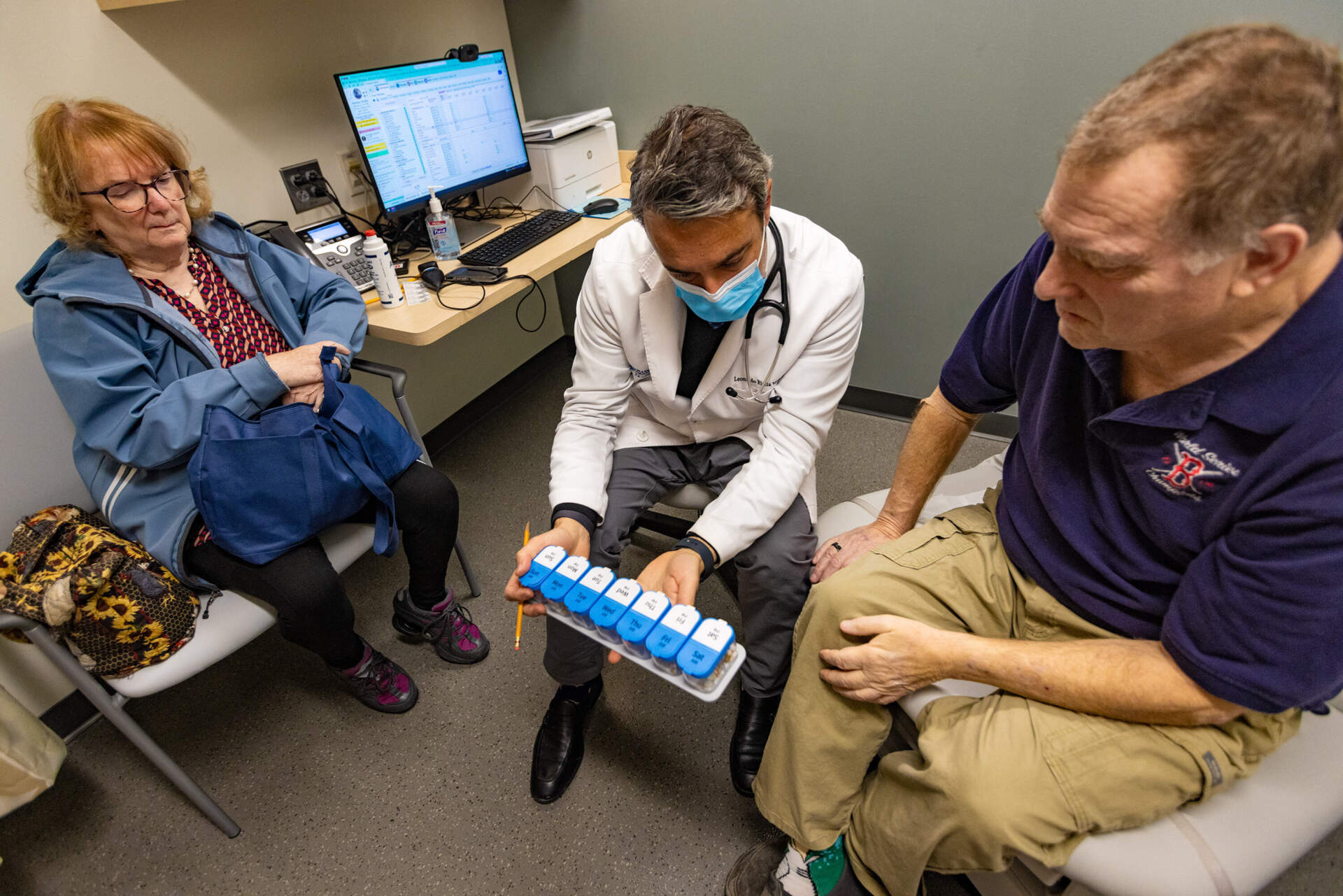 Dr. Leonardo Riella, center, reviews the weekly medications Tim Andrews needs to take with him and his wife, Karen. (Jesse Costa/WBUR)