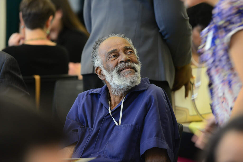 A portrait of Mel King, a Black man, seated and looking over his left shoulder with a smile.