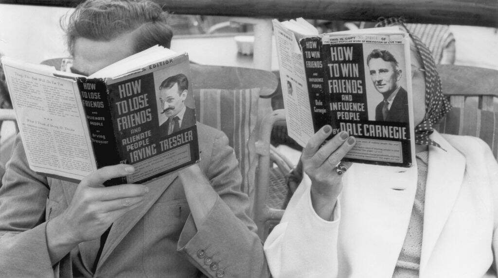 A man and a woman seated in deck chairs read contrasting 'How To' books, (one book is fictional,) held up to cover their faces, circa 1955. The man reads, 'How to Lose Friends and Alienate People,' by Irving Tressler; the woman reads, 'How to Win Friends and Influence People,' by Dale Carnegie. (Photo by Frederic Hamilton/Hulton Archive/Getty Images)