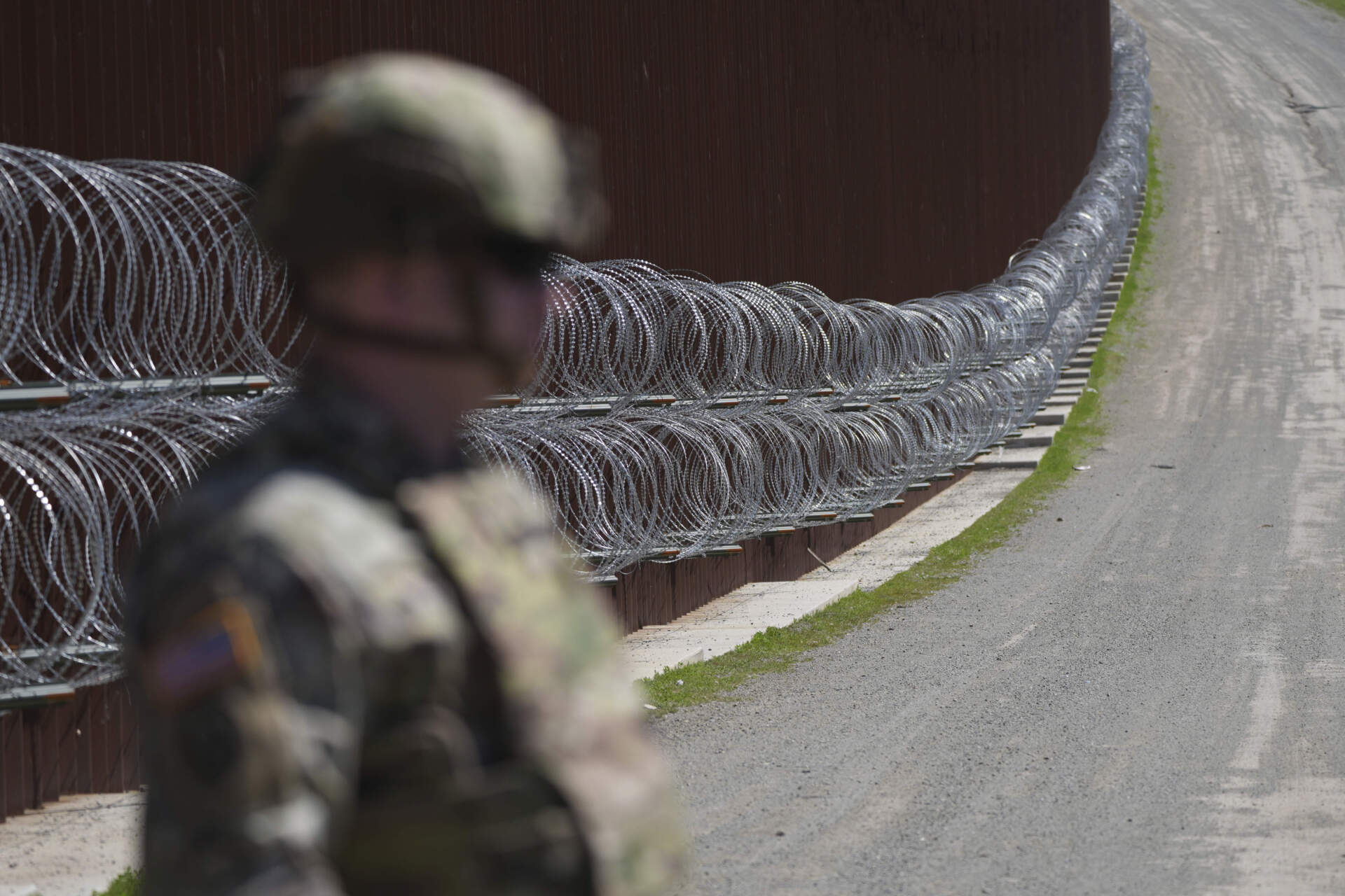 A member of the military looks on in front of newly-installed concertina wire lining one of two border walls separating Mexico from the United States on March 21. (Gregory Bull/AP)