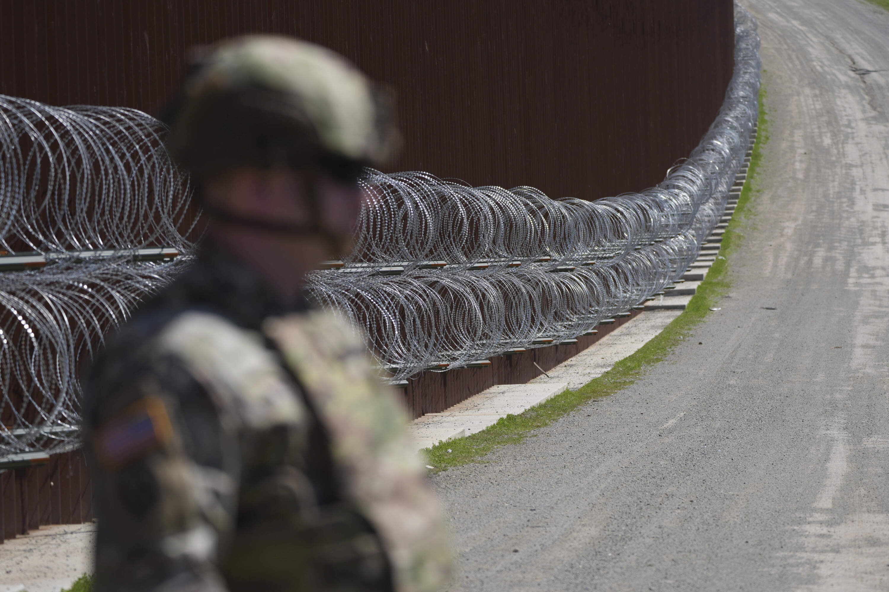 A member of the military looks on in front of newly-installed concertina wire lining one of two border walls separating Mexico from the United States on March 21. (Gregory Bull/AP)