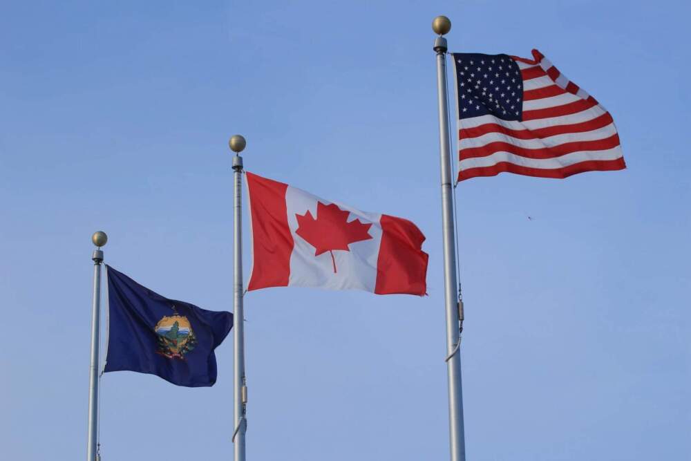 Flags for Vermont, Canada and the United States fly near Lake Memphremagog in Newport on Friday, Feb. 28, 2025. (Zoe McDonald/Vermont Public)