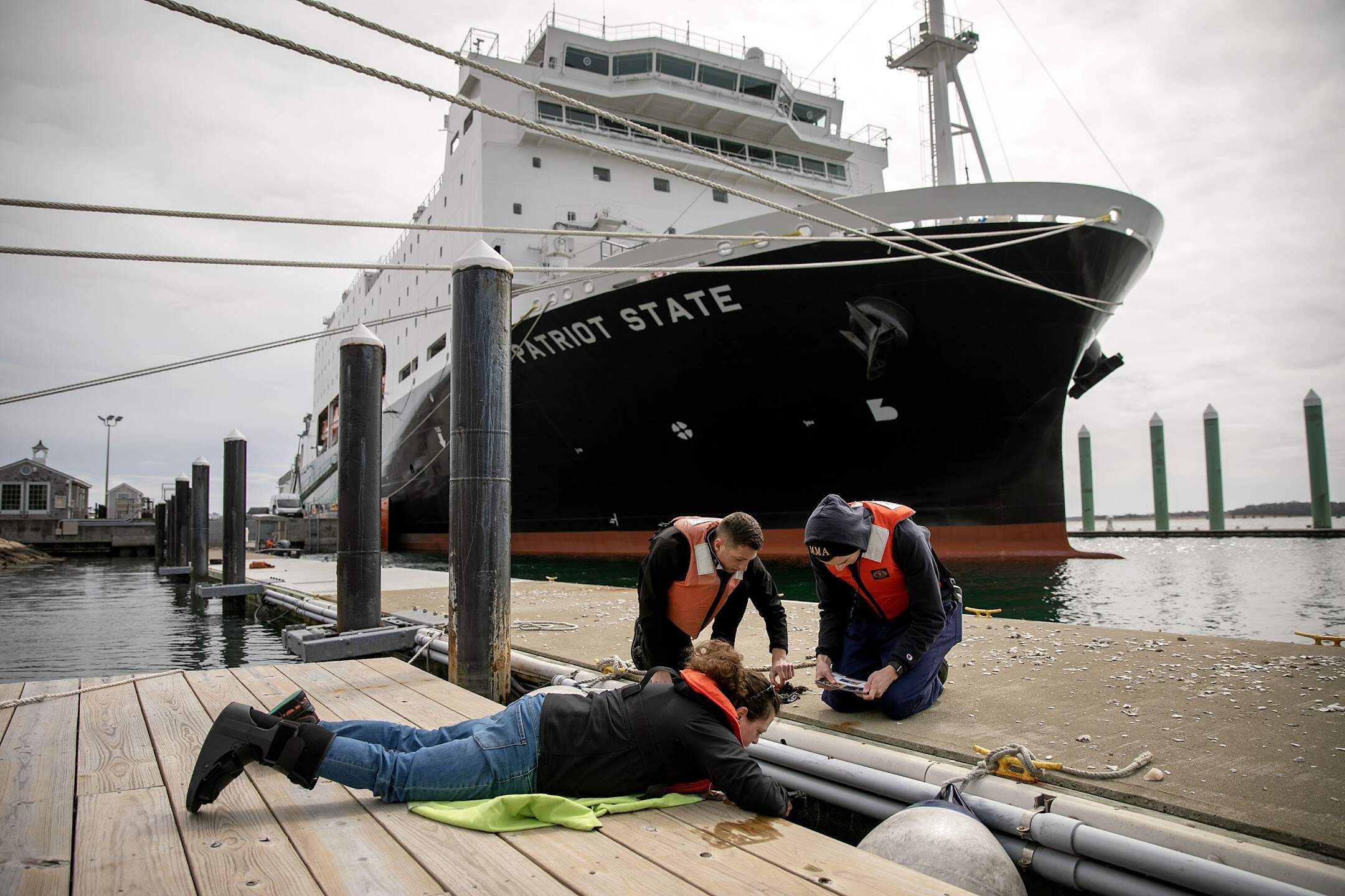 Kristin Osborne, an assistant professor at Massachusetts Maritime Academy, works with students to find and identify sea squirts on an academy pier. (Robin Lubbock/WBUR)