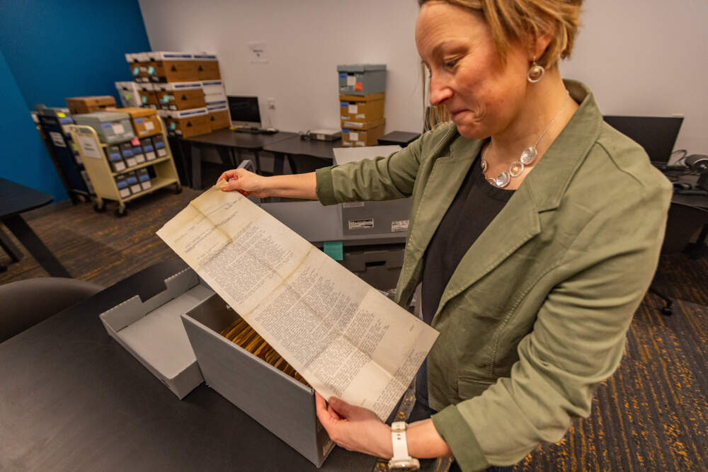 The author looks at the obituary of Boston Globe film critic Marjory Adams on teletype paper from 1980. (Jesse Costa/WBUR)