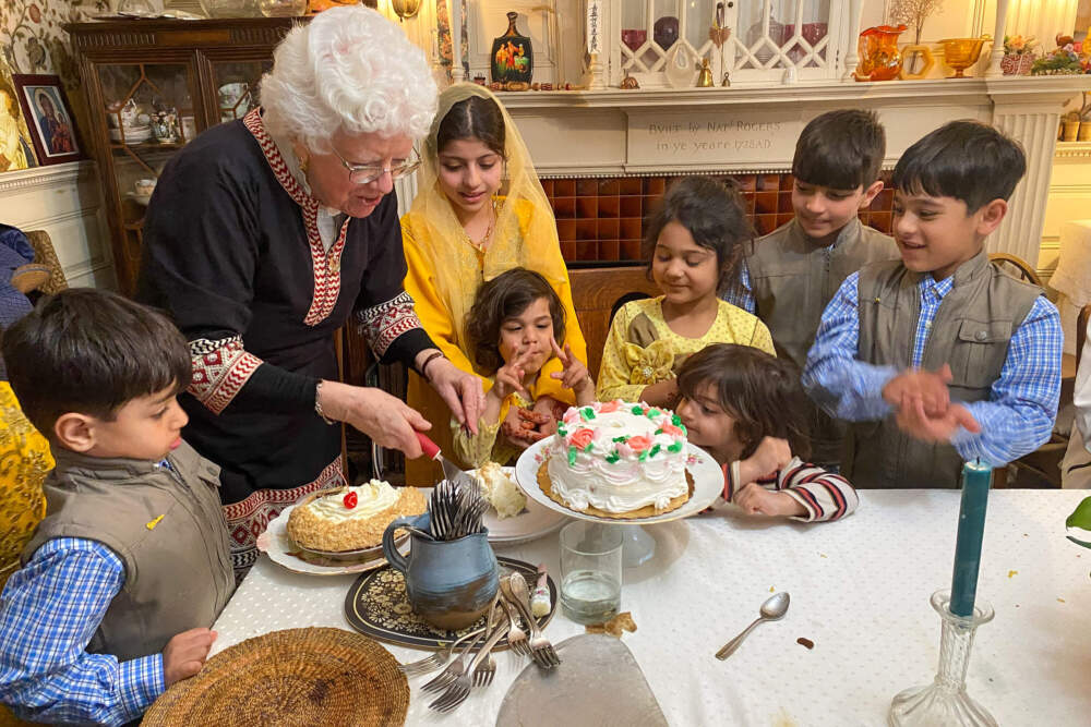 Afghan children gather around House of Peace Director Carrie Schuchardt as she prepares dessert for Eid festivities. (Deborah Becker/WBUR)