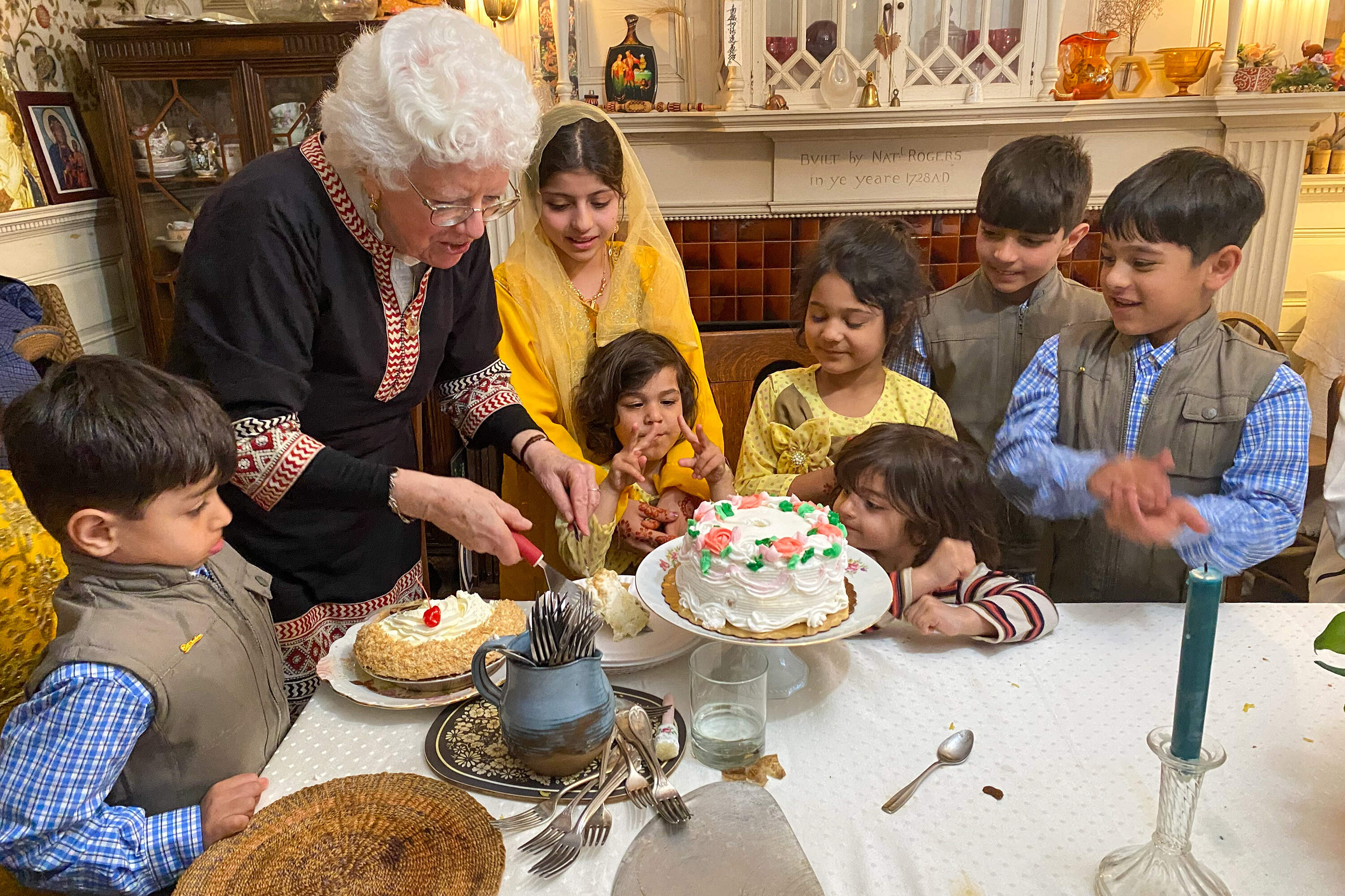 Afghan children gather around House of Peace Director Carrie Schuchardt as she prepares dessert for Eid festivities. (Deborah Becker/WBUR)
