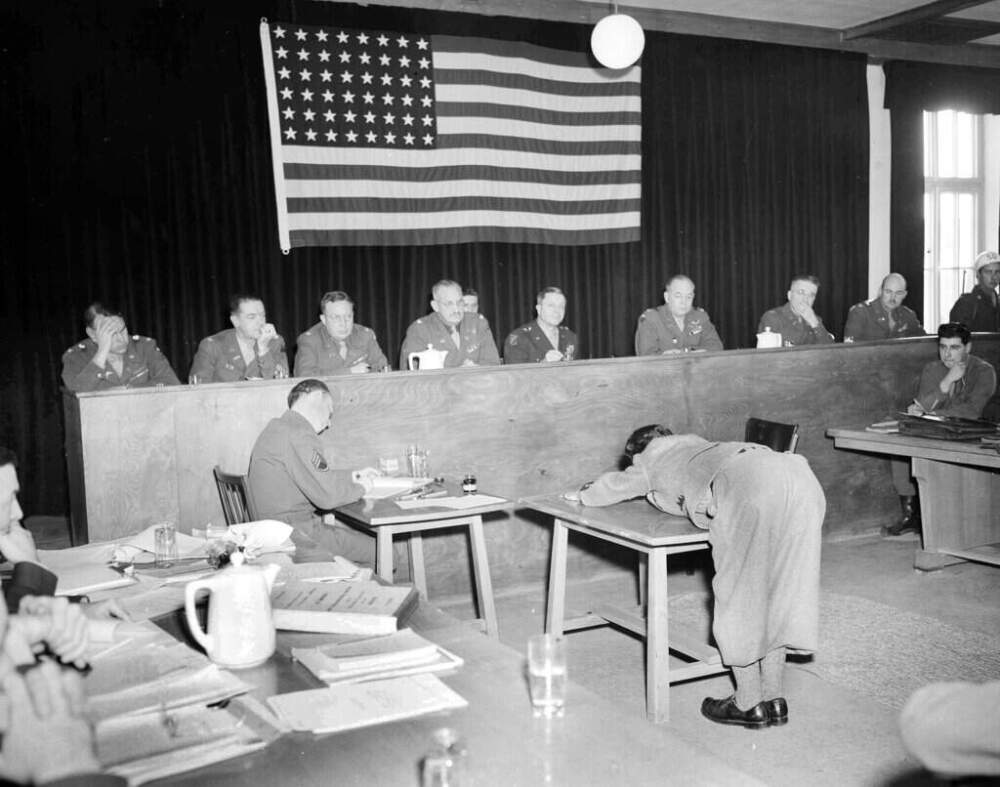 Rudolf Wolf, an engraver by trade, who was imprisoned at the Dachau concentration camp, demonstrates before the court the position prisoners had to assume when beatings were administered, during the Dachau War Crimes Trials held at the former concentration camp in Germany, Nov. 22, 1945 (AP)