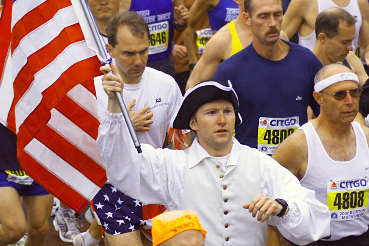 A runner in traditional colonial garb carries a flag past the starting line in the 106th Boston Marathon Monday, April 15, 2002 in Hopkinton, Mass. (Victoria Arocho/AP)
