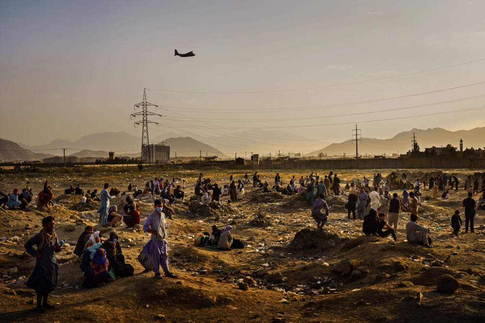 A military transport plane departs overhead as Afghans hoping to leave the country wait outside the Kabul airport on Aug. 23, 2021. (Marcus Yam for the Los Angeles Times via Getty Images)