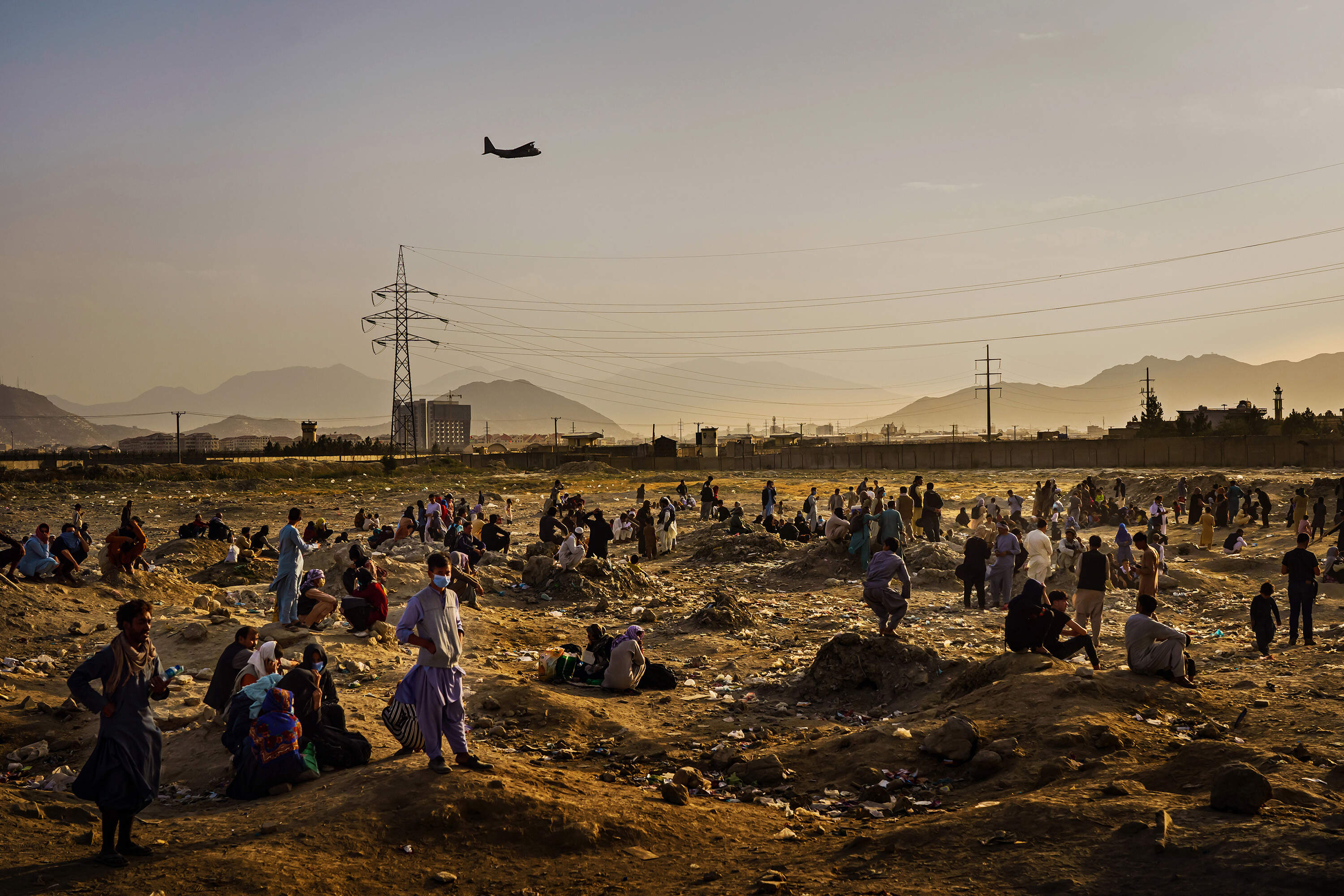 A military transport plane departs overhead as Afghans hoping to leave the country wait outside the Kabul airport on Aug. 23, 2021. (Marcus Yam for the Los Angeles Times via Getty Images)