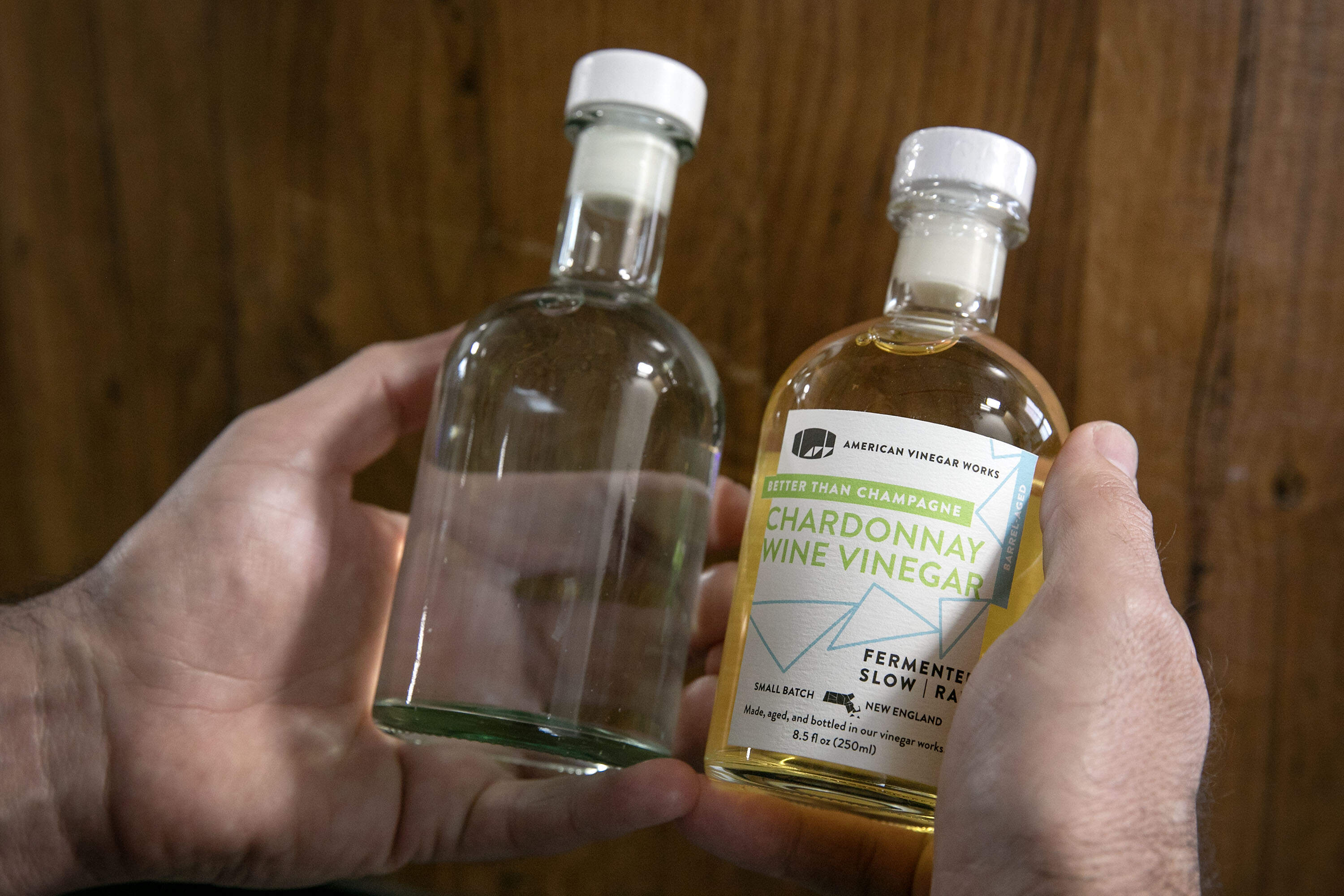 American Vinegar Works owner, Rodrigo Vargas, compares the new and old vinegar bottles, after tariffs made him look for a new supplier. (Robin Lubbock/WBUR)