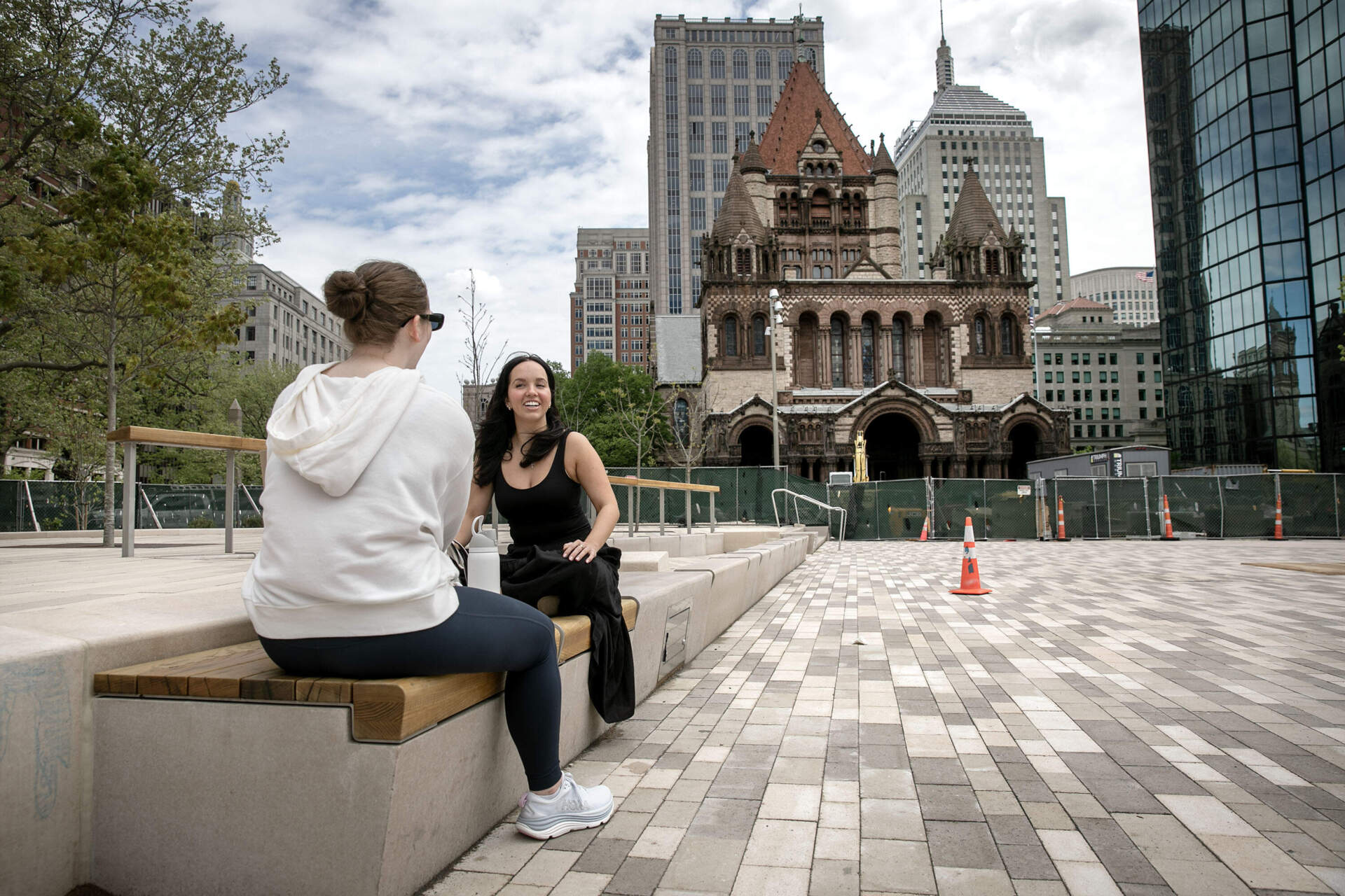 Sophie Skinner, who recently moved to Boston, talks with a friend on one the new wood benches on Copley Square Plaza. (Robin Lubbock/WBUR)