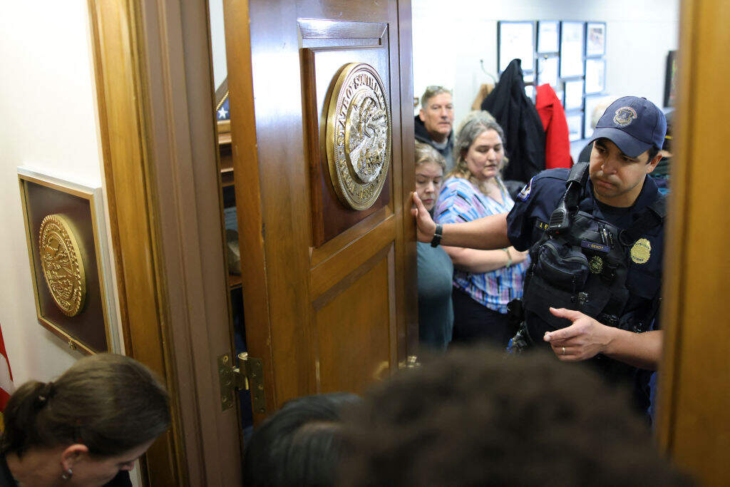 A U.S. Capitol Police officer closes an office door as federal employees affected by DOGE budget cuts and terminations enter the offices of U.S. Senator John Thune (R-SD) to request a meeting on February 25. ( Bryan Dozier/Middle East Images/AFP via Getty Images)