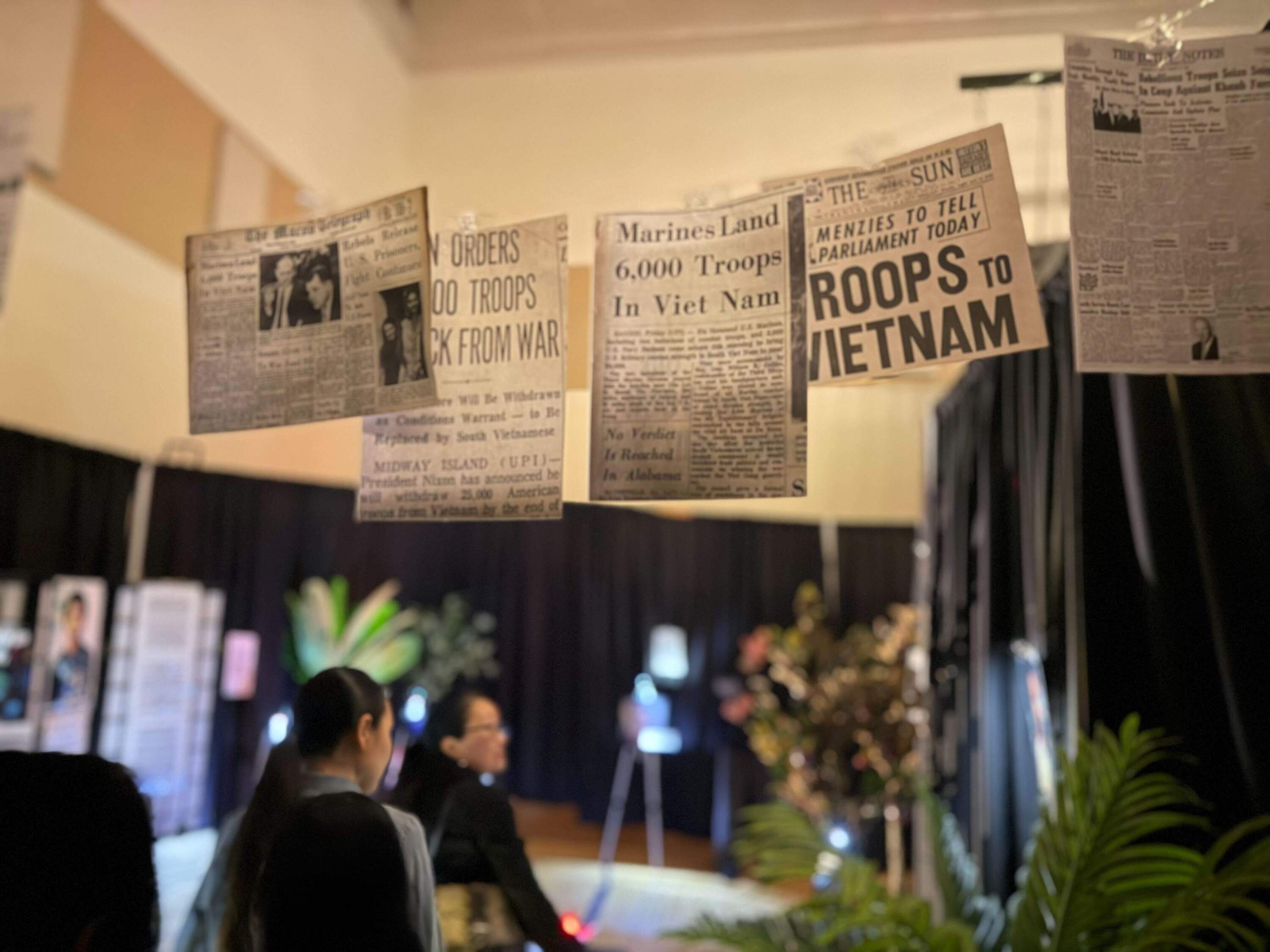 Thanh Nguyen and her daughter-in-law, Vy Vu enter the immersive exhibition, which opens with a passage filled with newspaper clippings from the Vietnam War. (Cristela Guerra/WBUR)