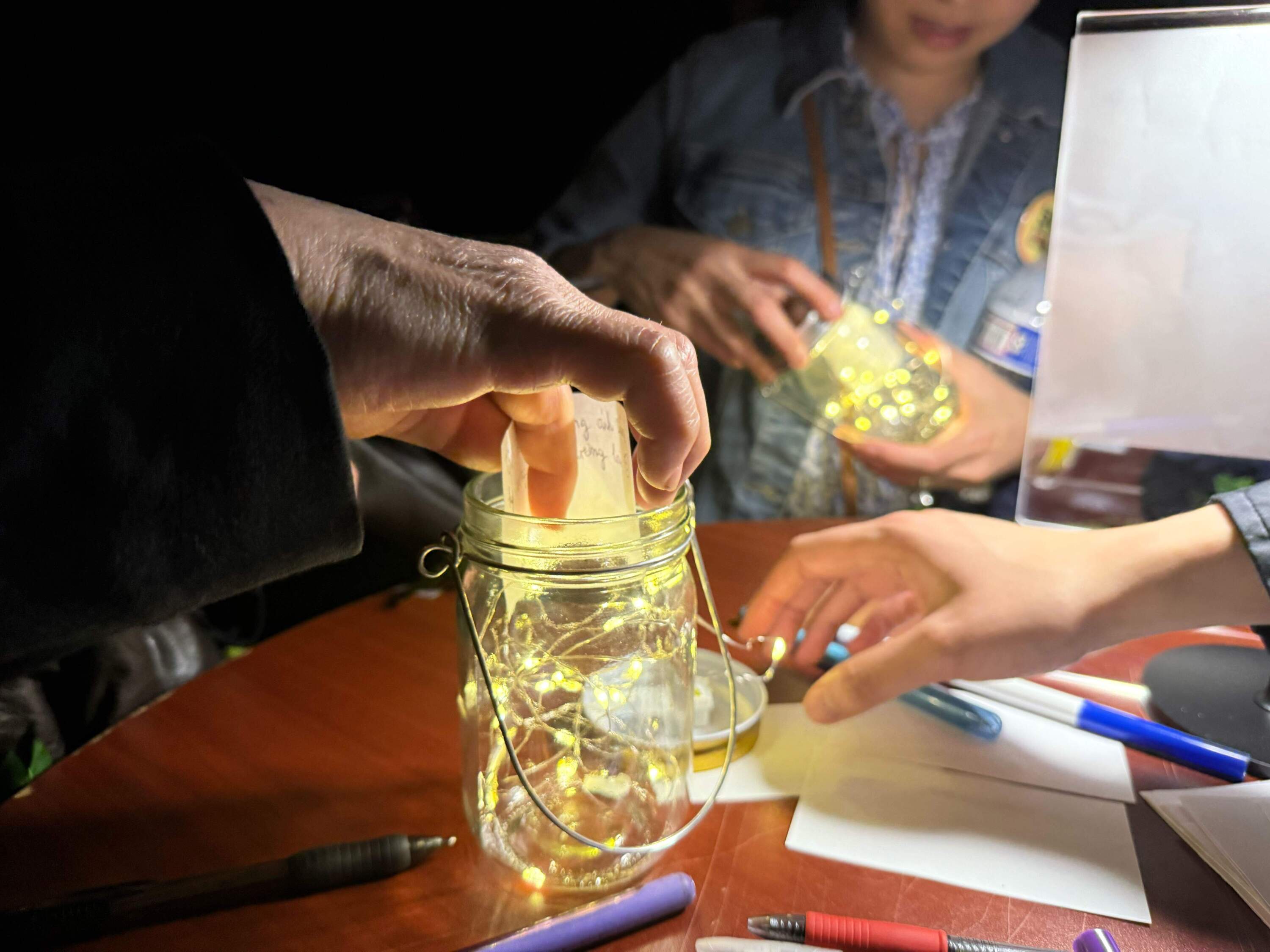 Thanh Nguyen and Vy Vu place notes inside their glowing jar, which symbolize fireflies, a main theme during the commemoration. (Cristela Guerra/WBUR)
