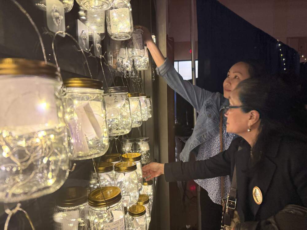 Thanh Nguyen and Vy Vu place glowing jars among others inside the immersive exhibition at Boston College High School in Dorchester. (Cristela Guerra/WBUR)