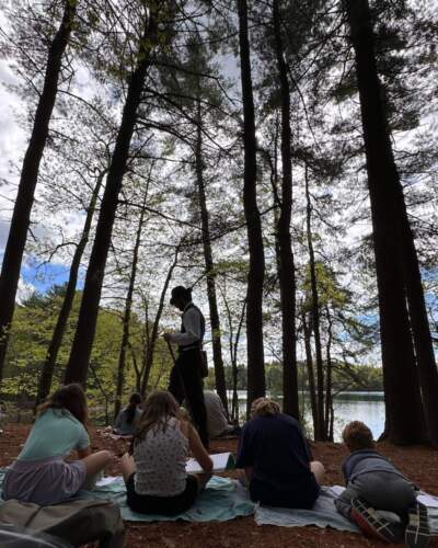 Children sketch near Walden Pond, as an employee, playing the role of Henry David Thoreau, walks by. (Courtesy Cloe Axelson)