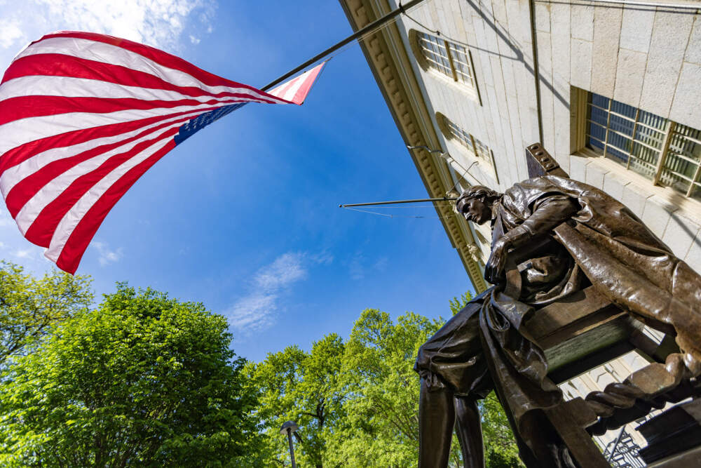 An American Flag flies over the statue of John Harvard in Harvard Yard. (Jesse Costa/WBUR)